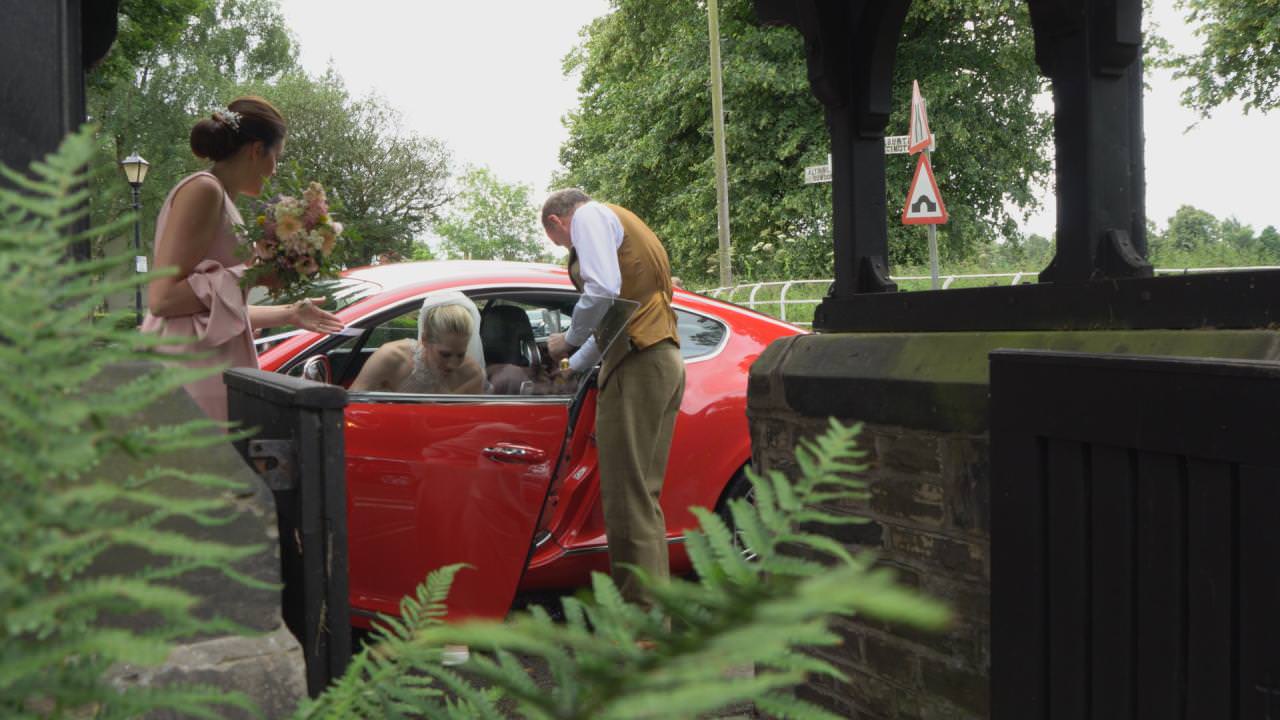 a bride steps out of a red sports car outside St Marks Church