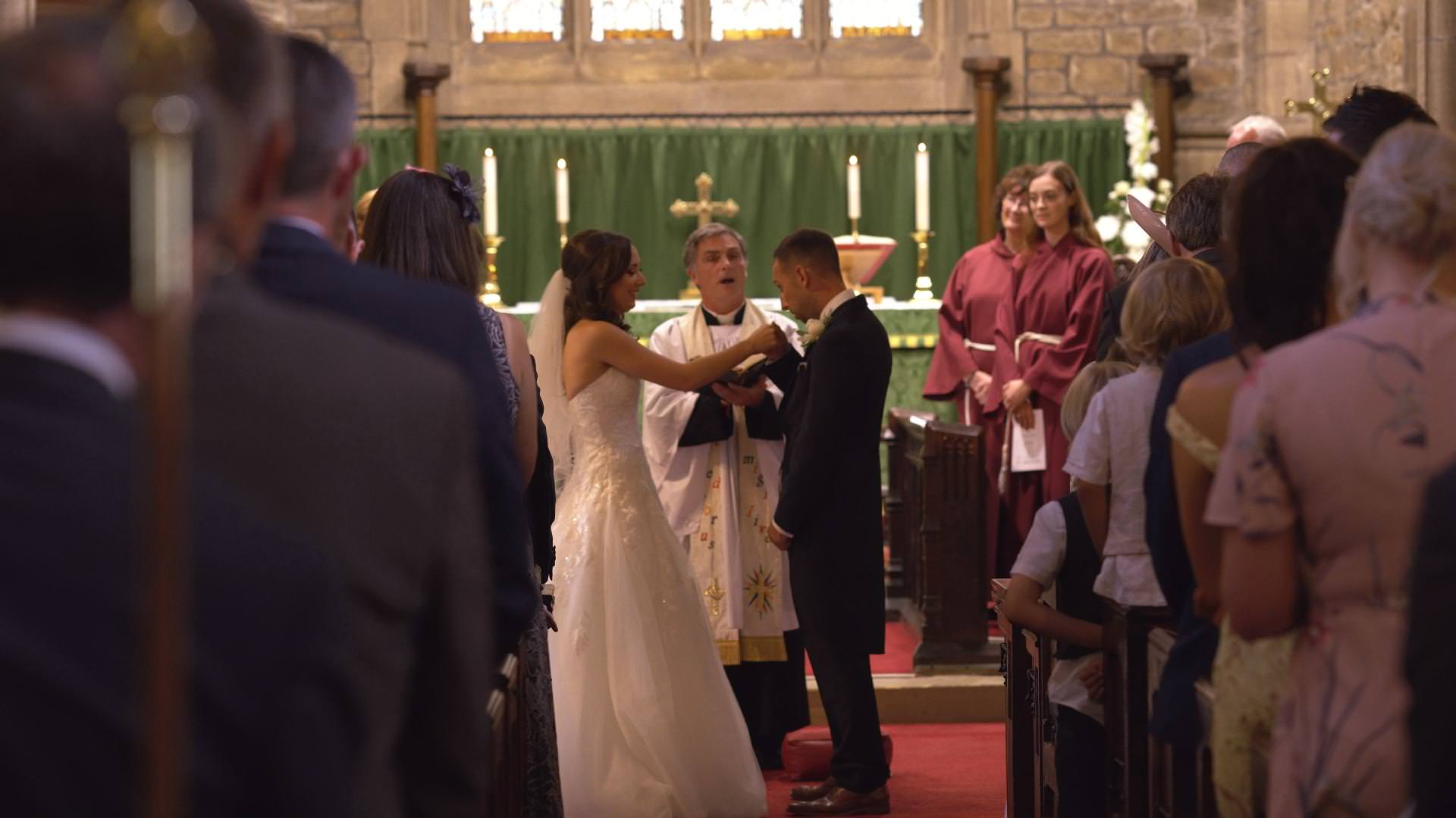 the groom coughs on to the brides hand during vows at St Bartholomews and St John’s Church,