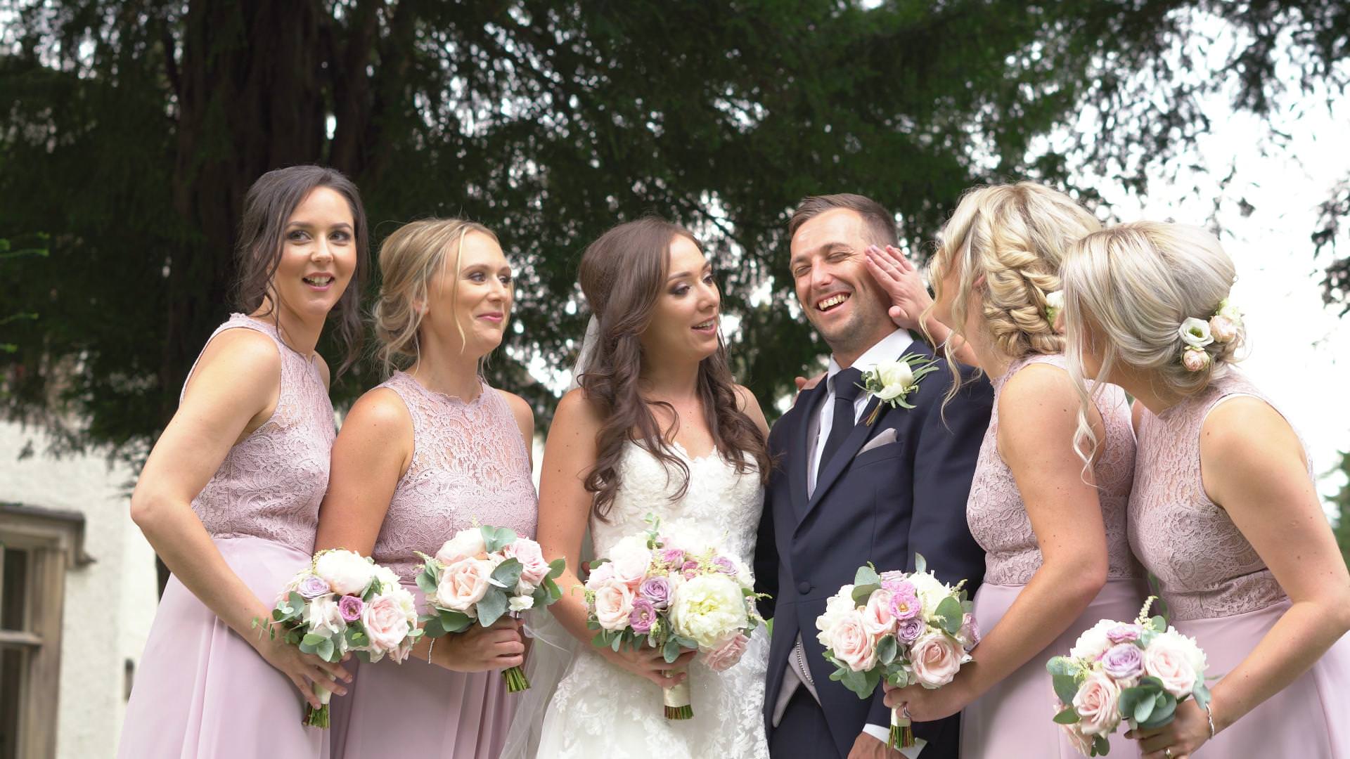 the groom laughs as the bridesmaids fuss over him during wedding photos at Mitton Hall