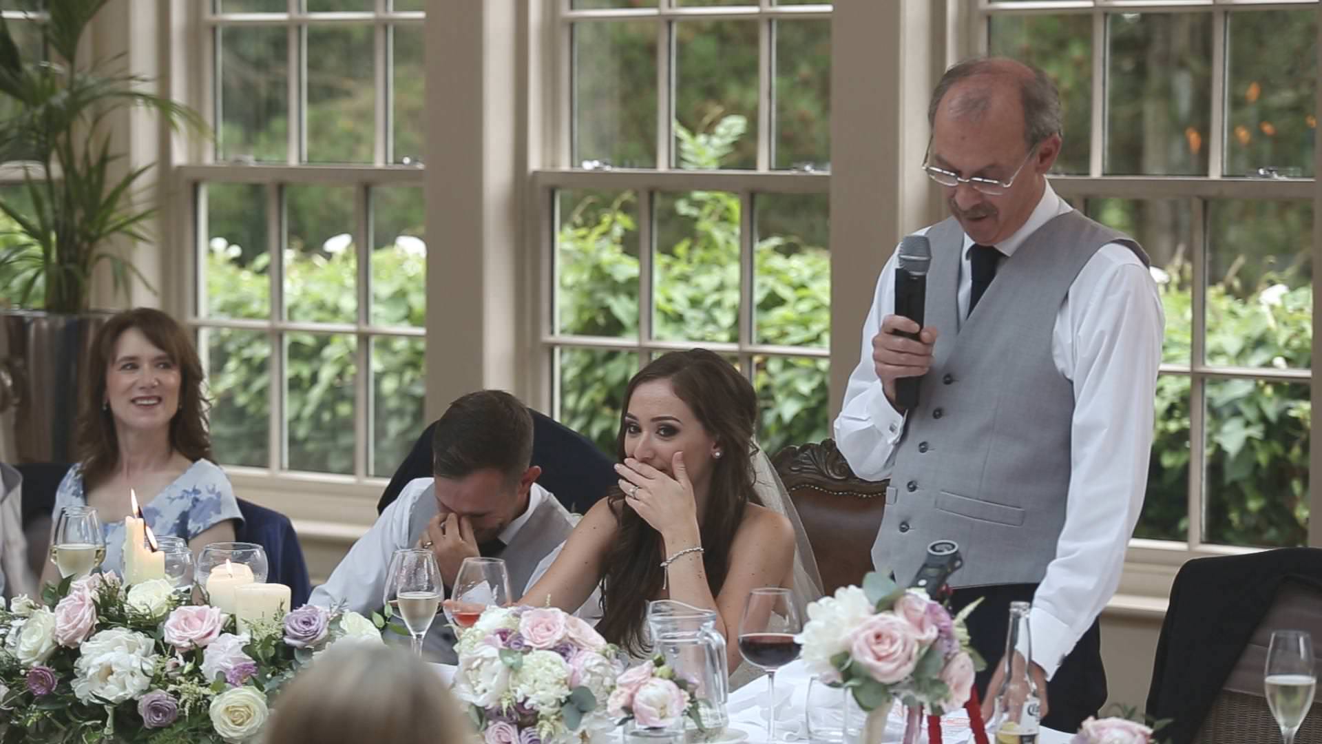 a bride and groom hide their faces during a father of the bride speech at mitton hall