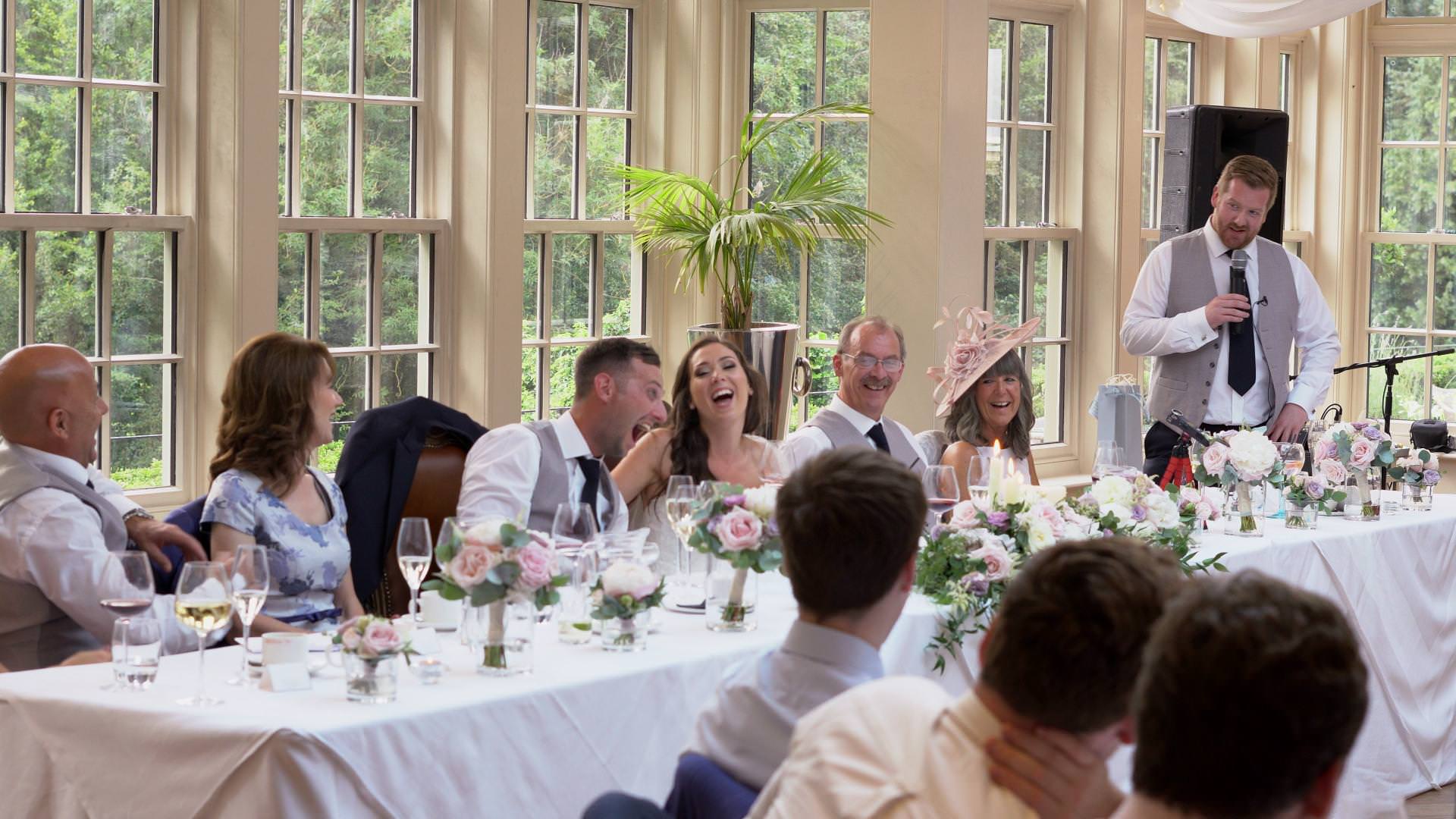a wedding video still of the whole top table laughing during a best man speech at Mitton hall