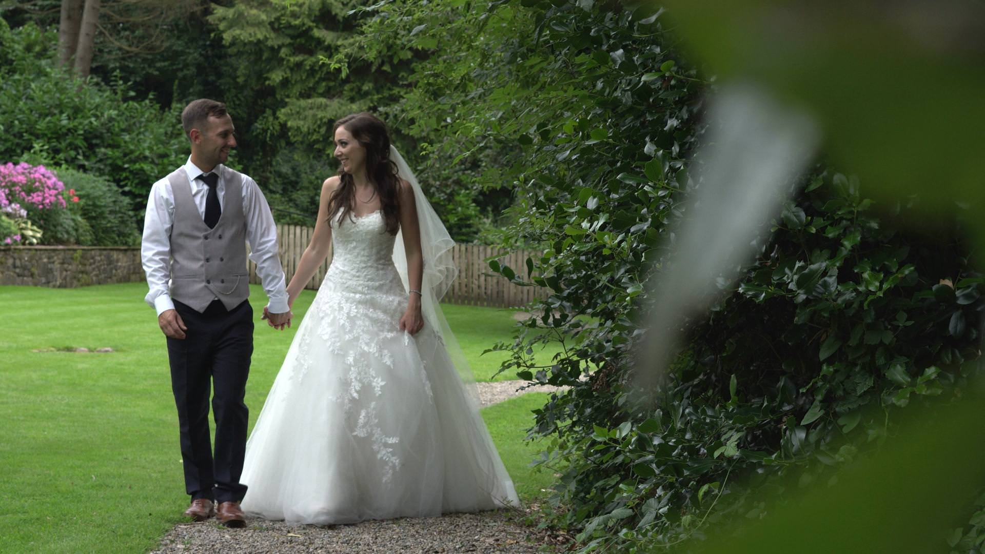 a bride and groom hold hands and walk around mitton hall for photographs