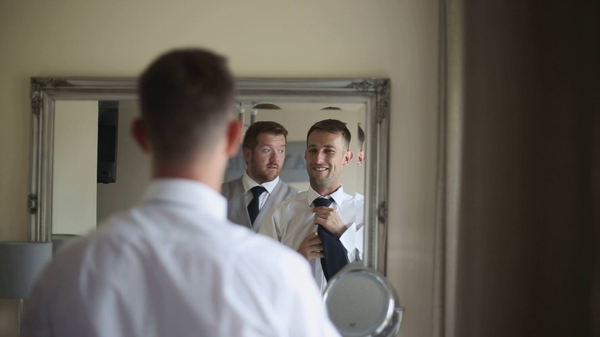 a wedding video still of a groom and best man doing their ties in the mirror in Lancashire