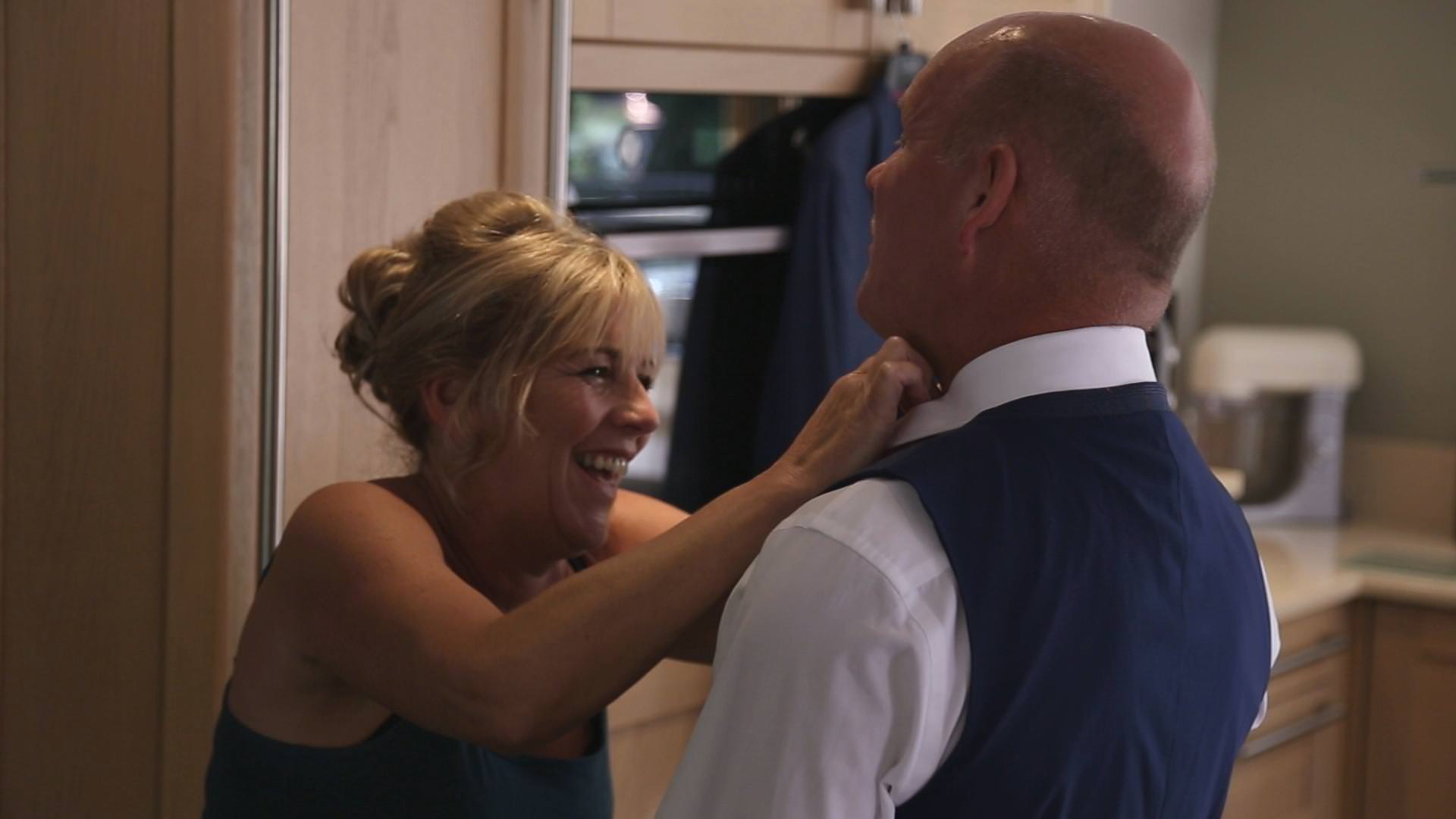 a wedding video still of a mother of the groom laughing at her husband