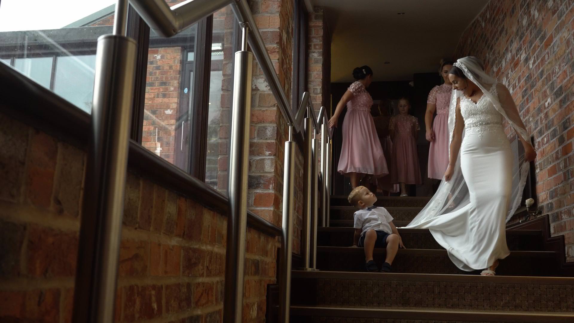 a bride makes her way to the ceremony room passing a sitting page boy at Moddershall