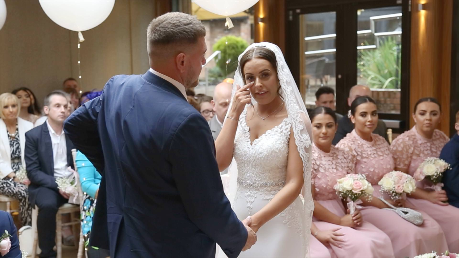 video still of a bride wiping away a tear during a Moddershall Oaks indoor ceremony