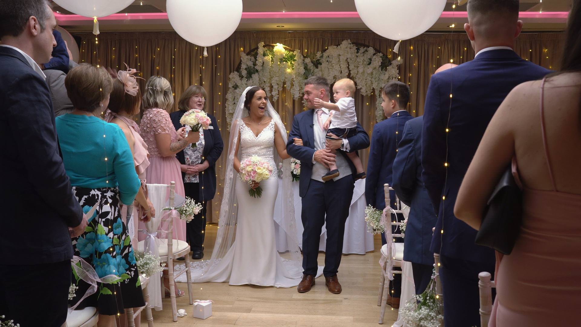 a bride and groom wait to walk down the aisle holding their baby boy in Staffordshire