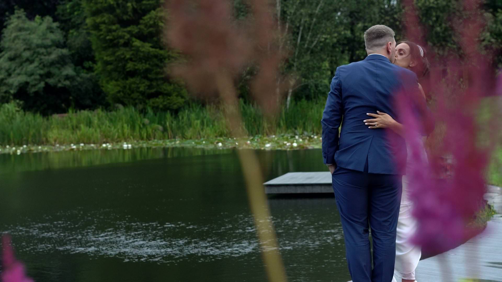 a bride and groom kiss on the lake at Moddershall Oaks