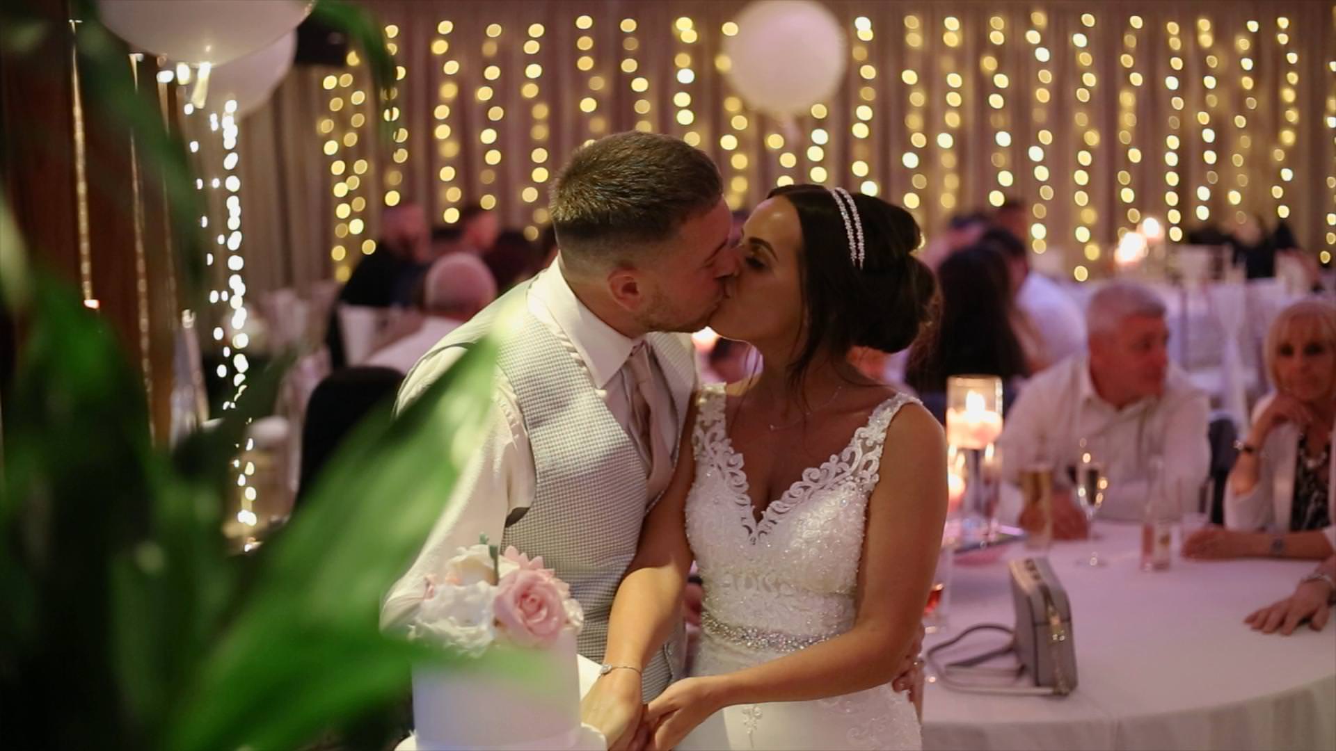 a bride and groom kiss as they cut the cake for the wedding videographer at Moddershall Oaks