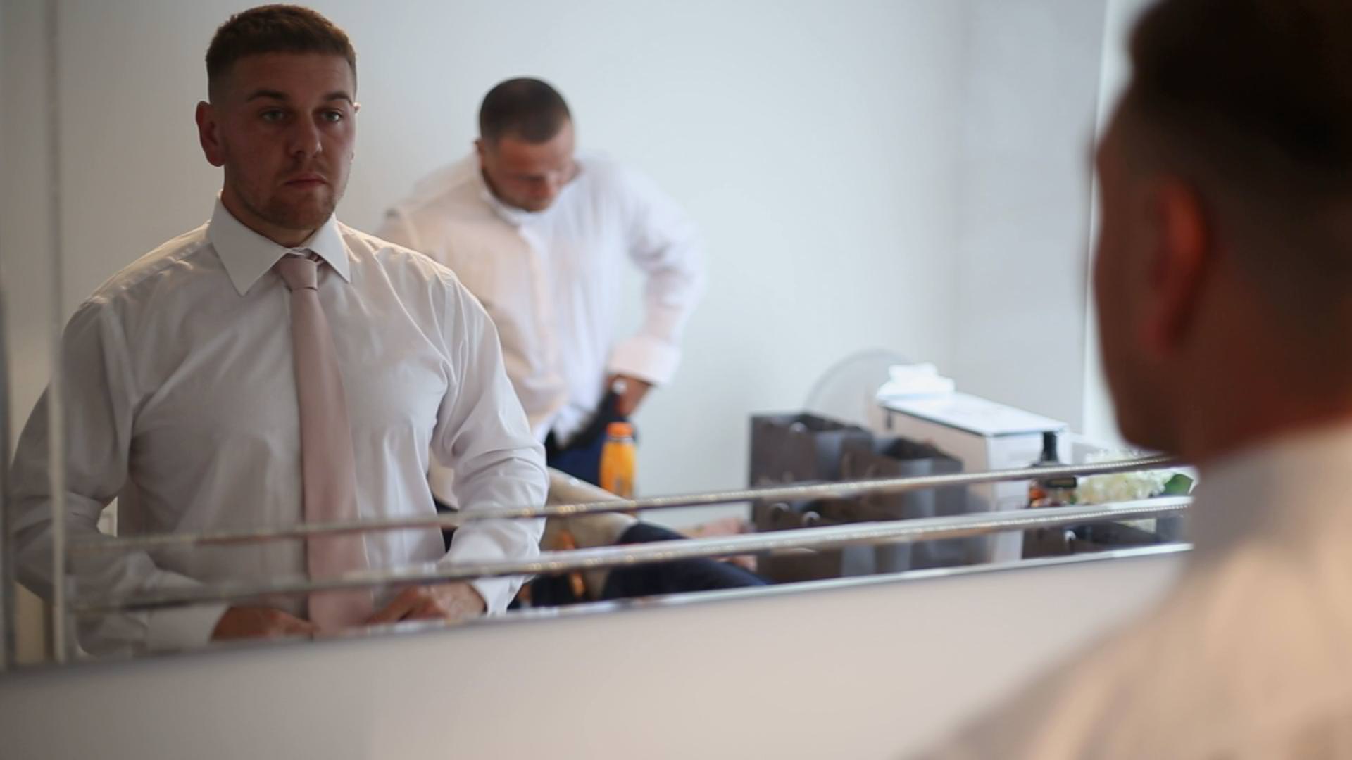 a video still of a groom getting ready in front of a mirror