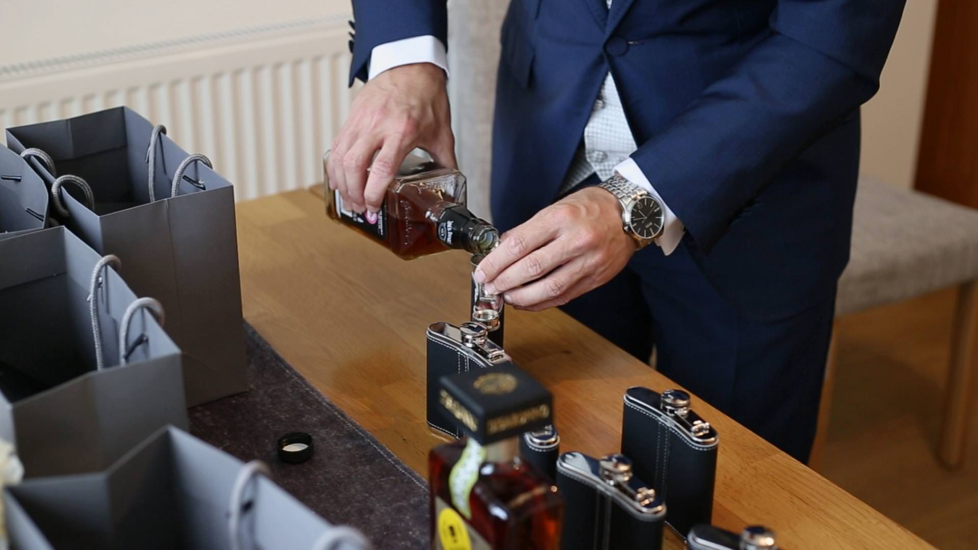 a close up video still of a groom pouring whisky in to wedding flask