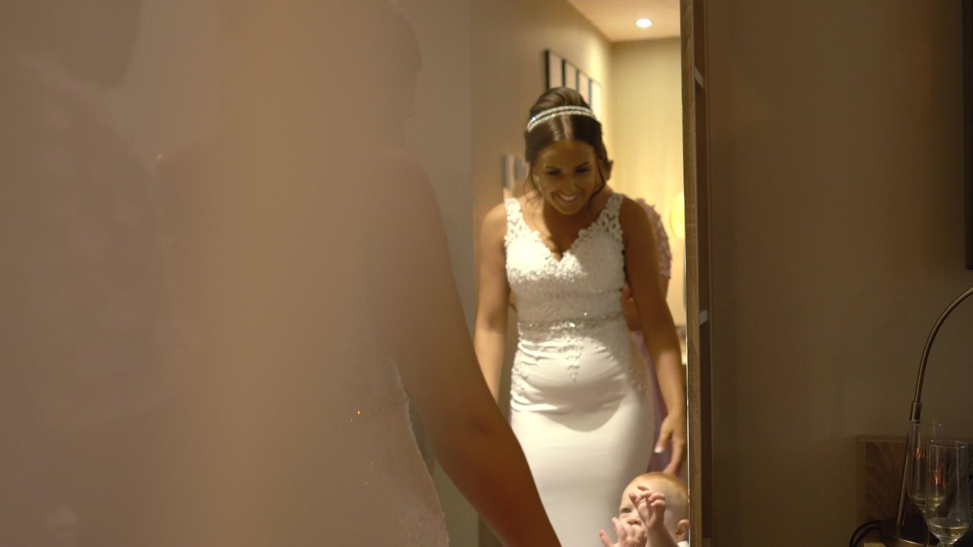 a bride smiles down at her son whilst getting in to her wedding dress at Moddershall Oaks