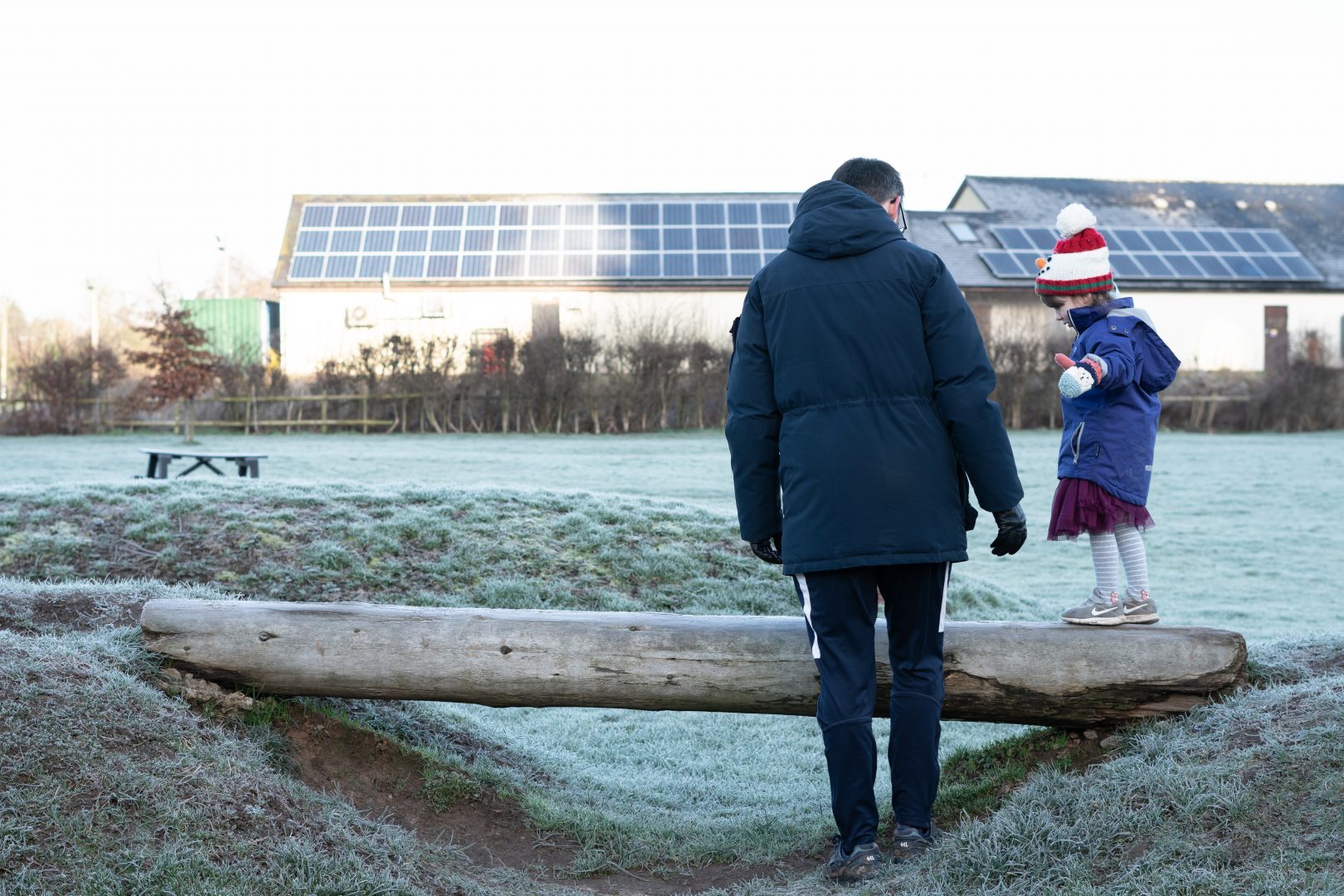 a photo of a dad and daughter play on a balance beam with thick winter frost