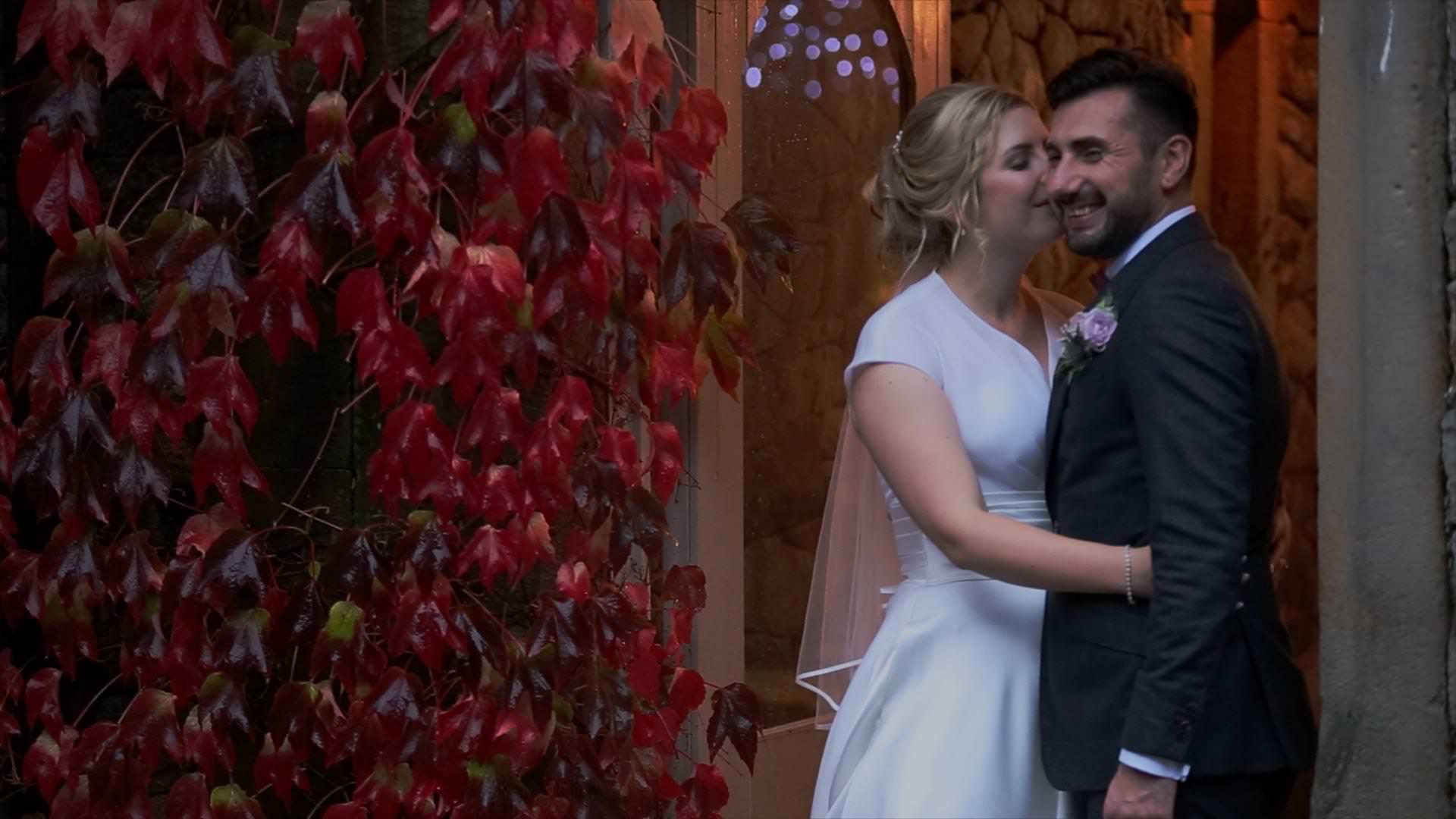 bride kisses groom on the cheek by autumnal red leaves