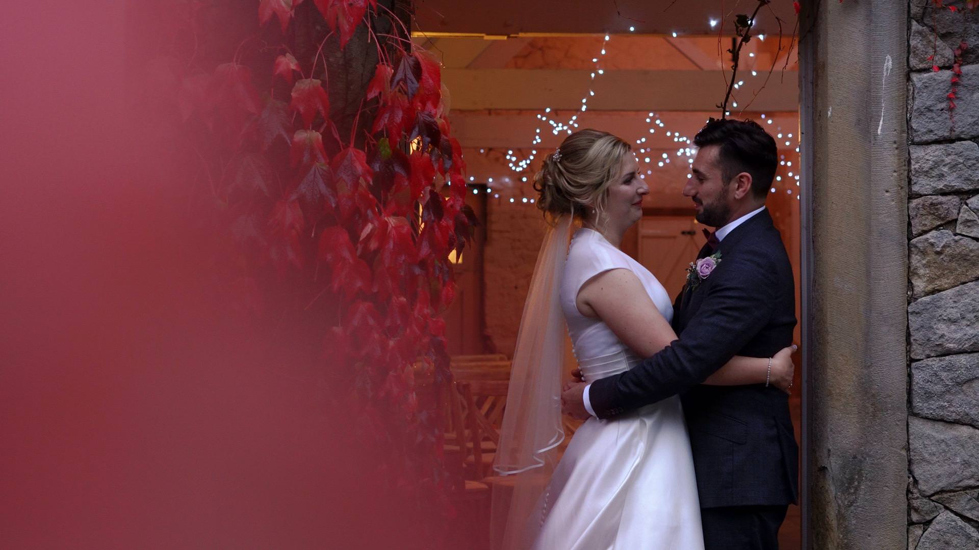 bride and groom cuddle by red leaves for wedding video