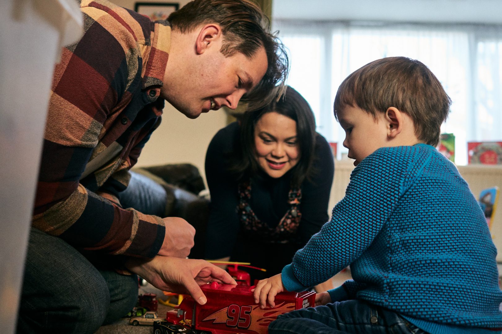 mum dad and 3 year old son sit close and look at cars