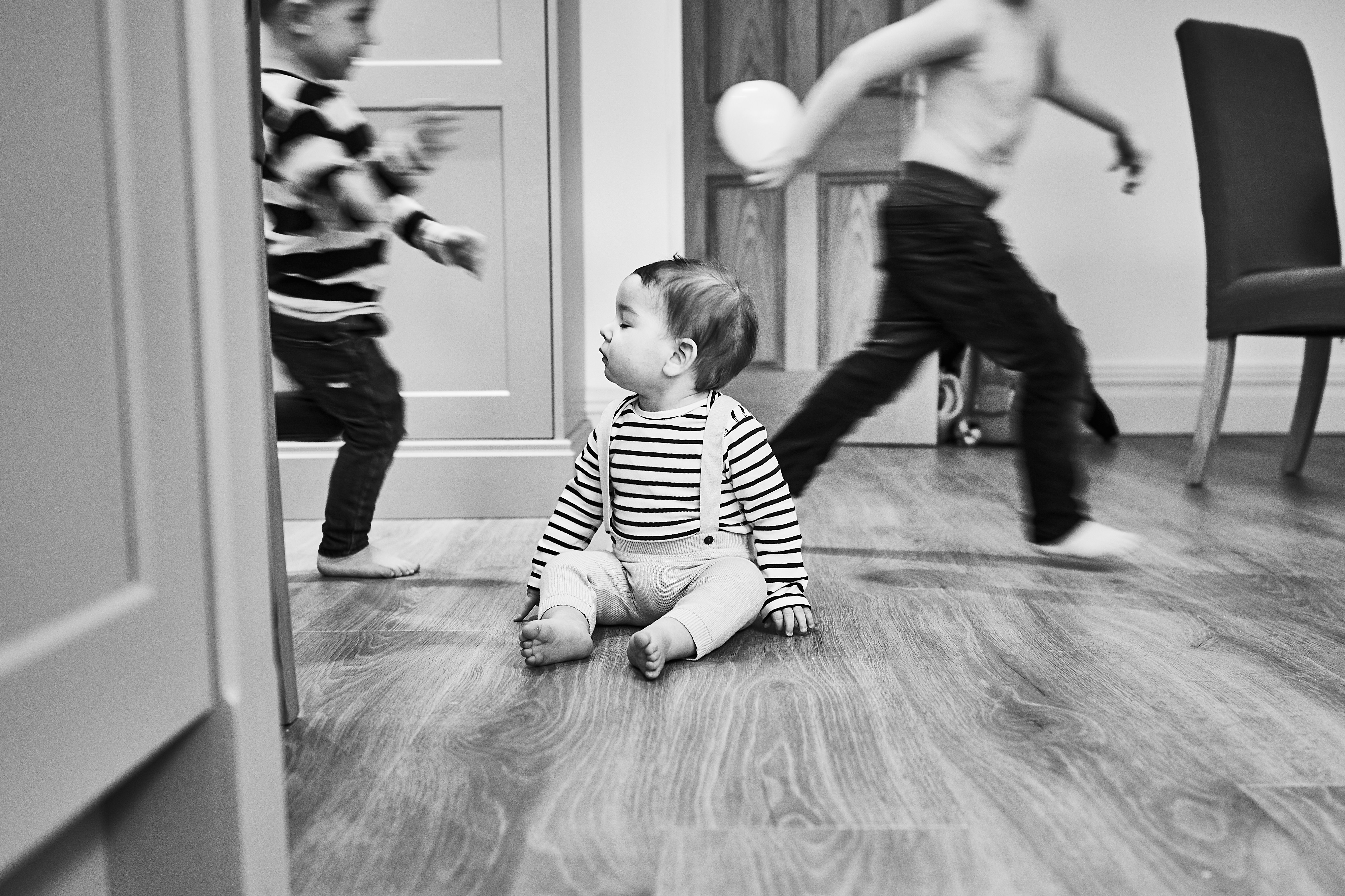 family photo of baby sitting on floor as older brothers run around him