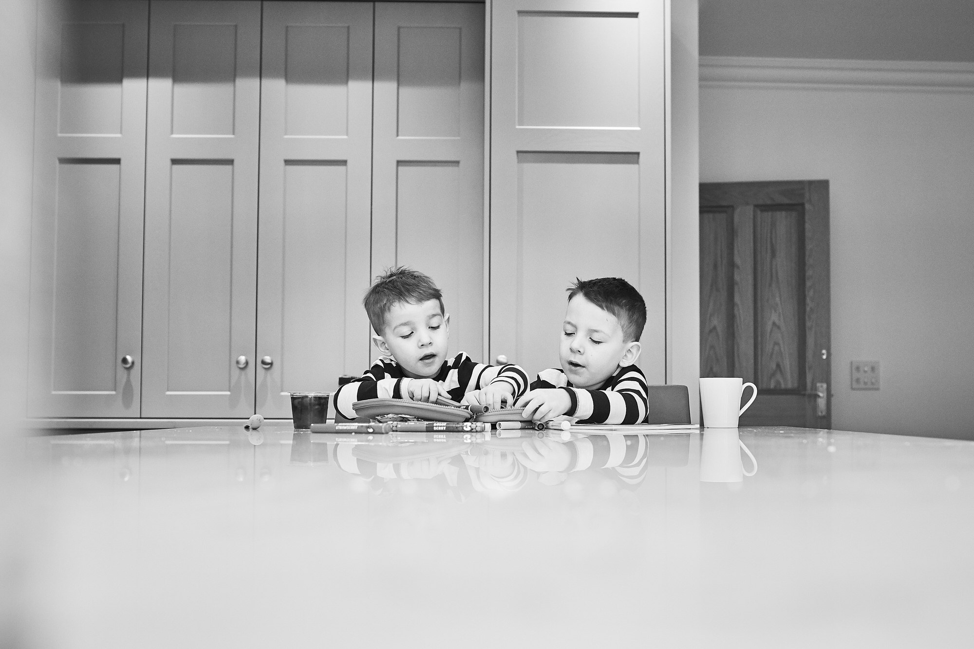 two boys sit at big kitchen table drawing