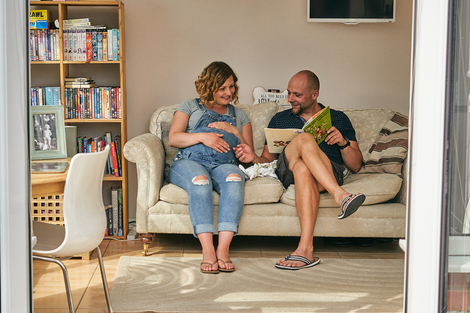 couple sit reading childrens book to bump at home