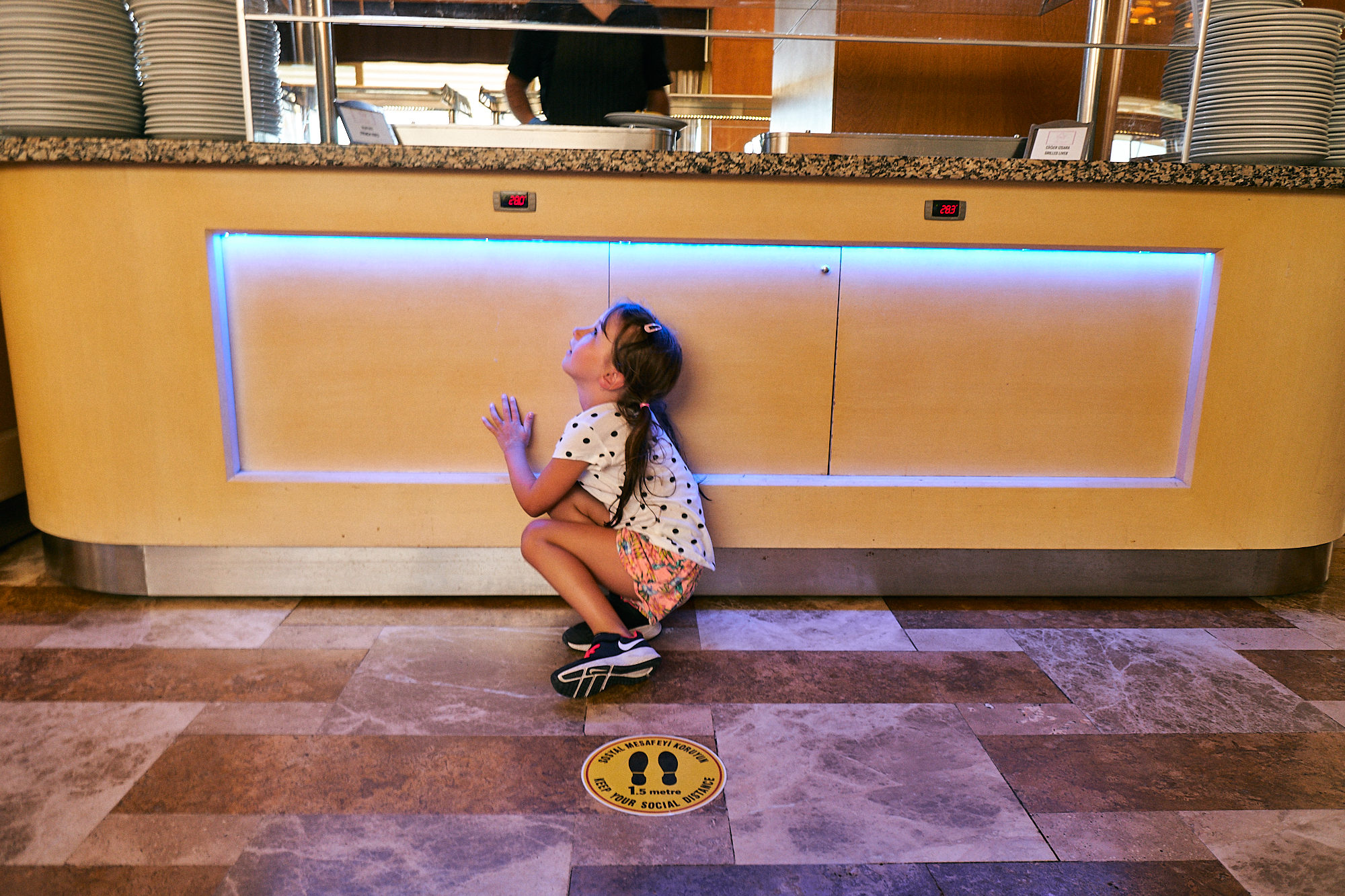 child hides by social distancing sign