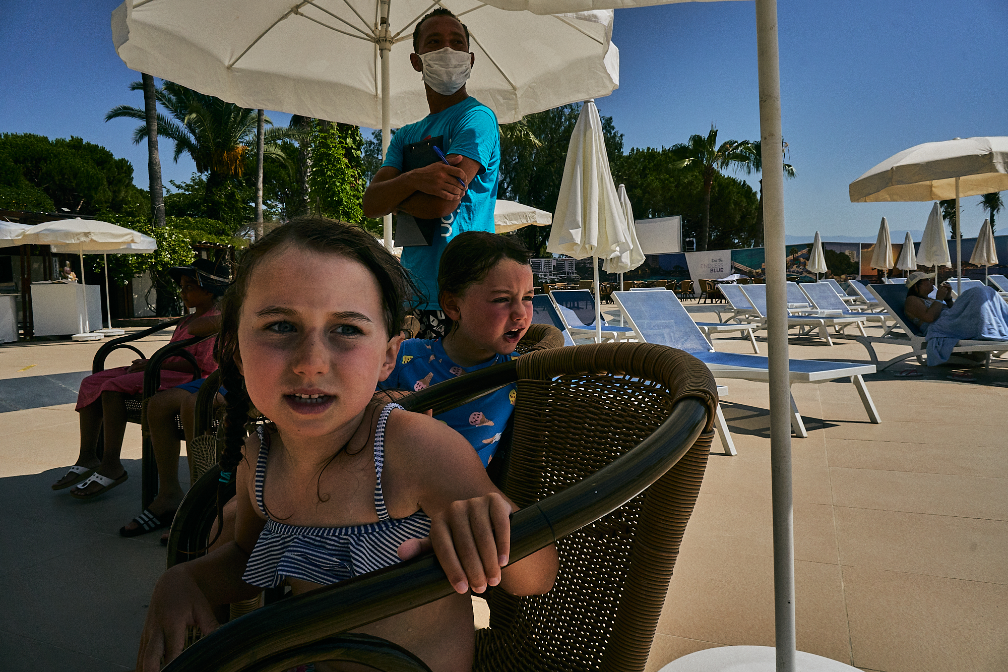 children sit by pool with staff in PPE on holiday
