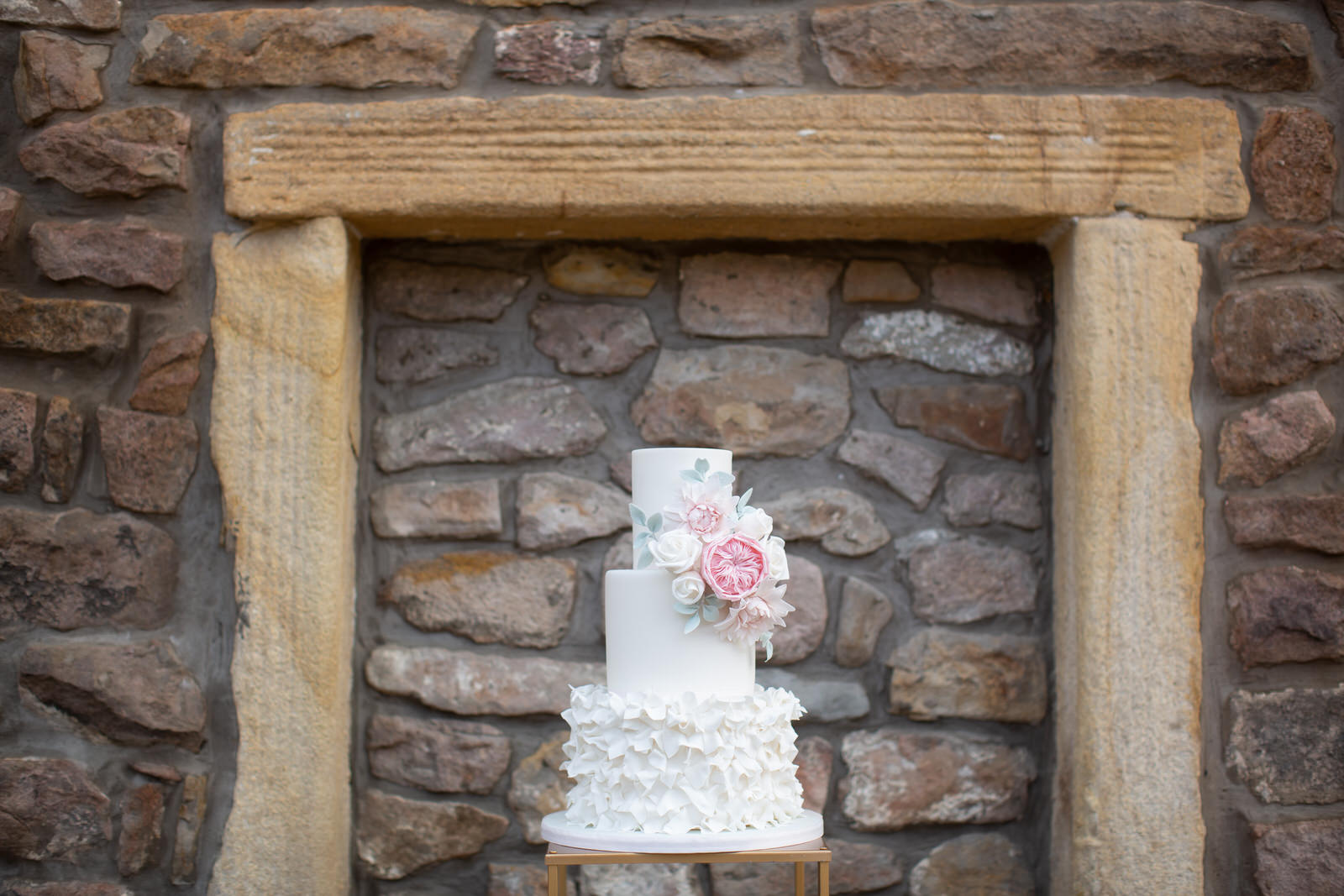 simple white wedding cake beside stone barn wall