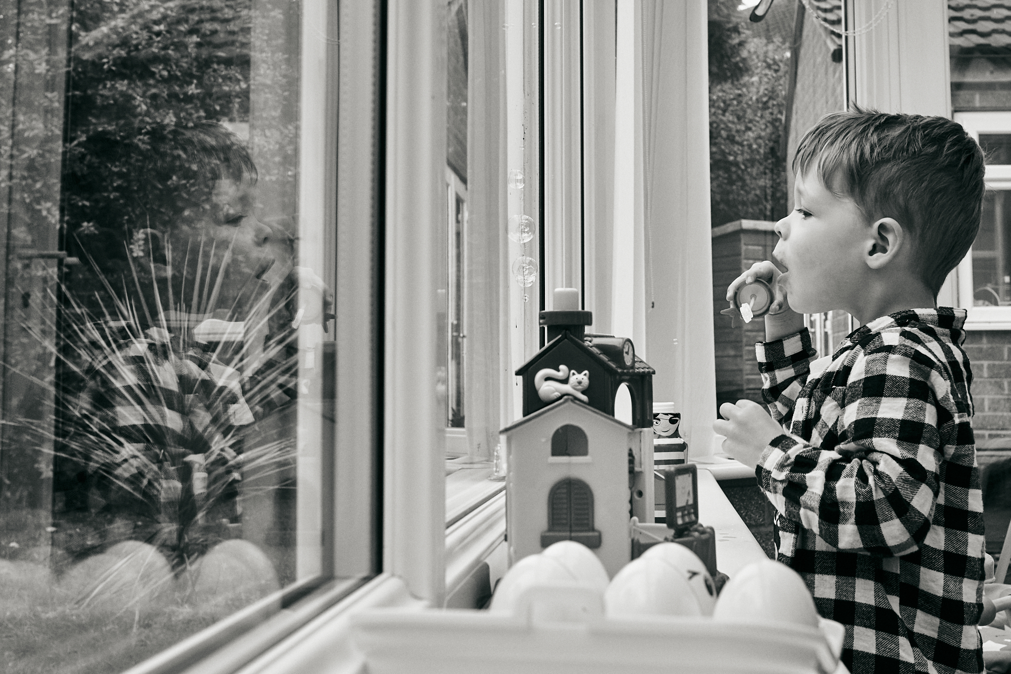 black and white photo child blowing bubbles at window
