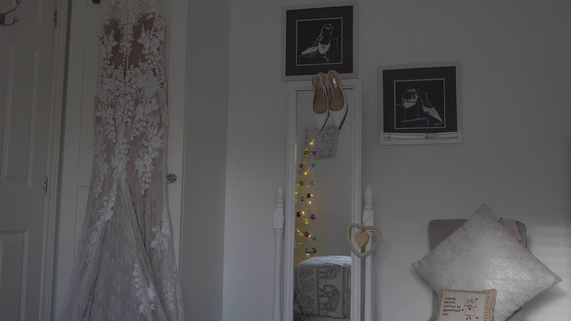 brides wedding dress hangs ready by mirror