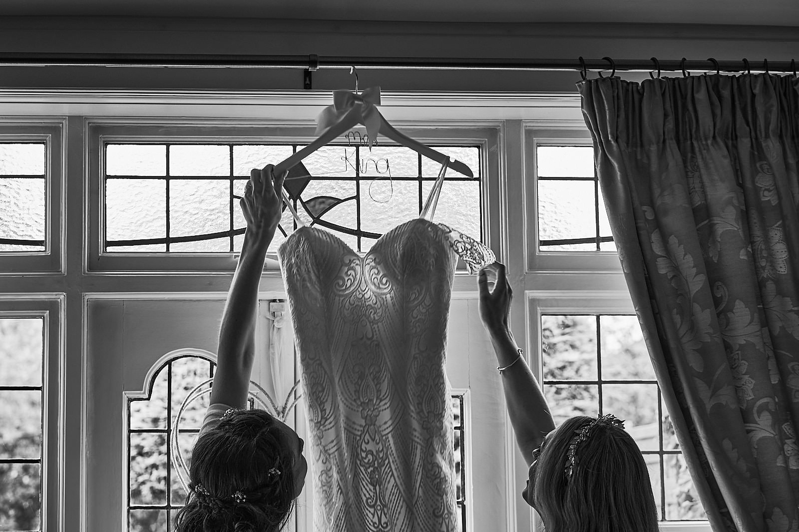 black and white photo of bride and sister reach for the wedding dress