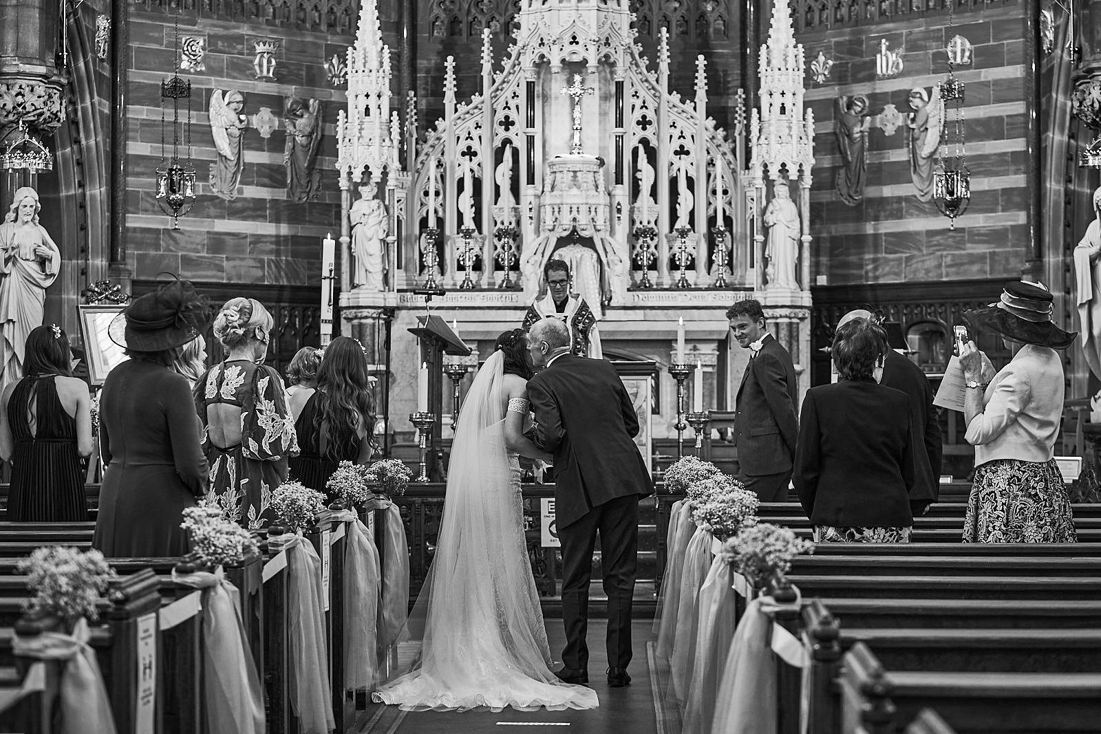 black and white candid photo of dad kissing bride in church