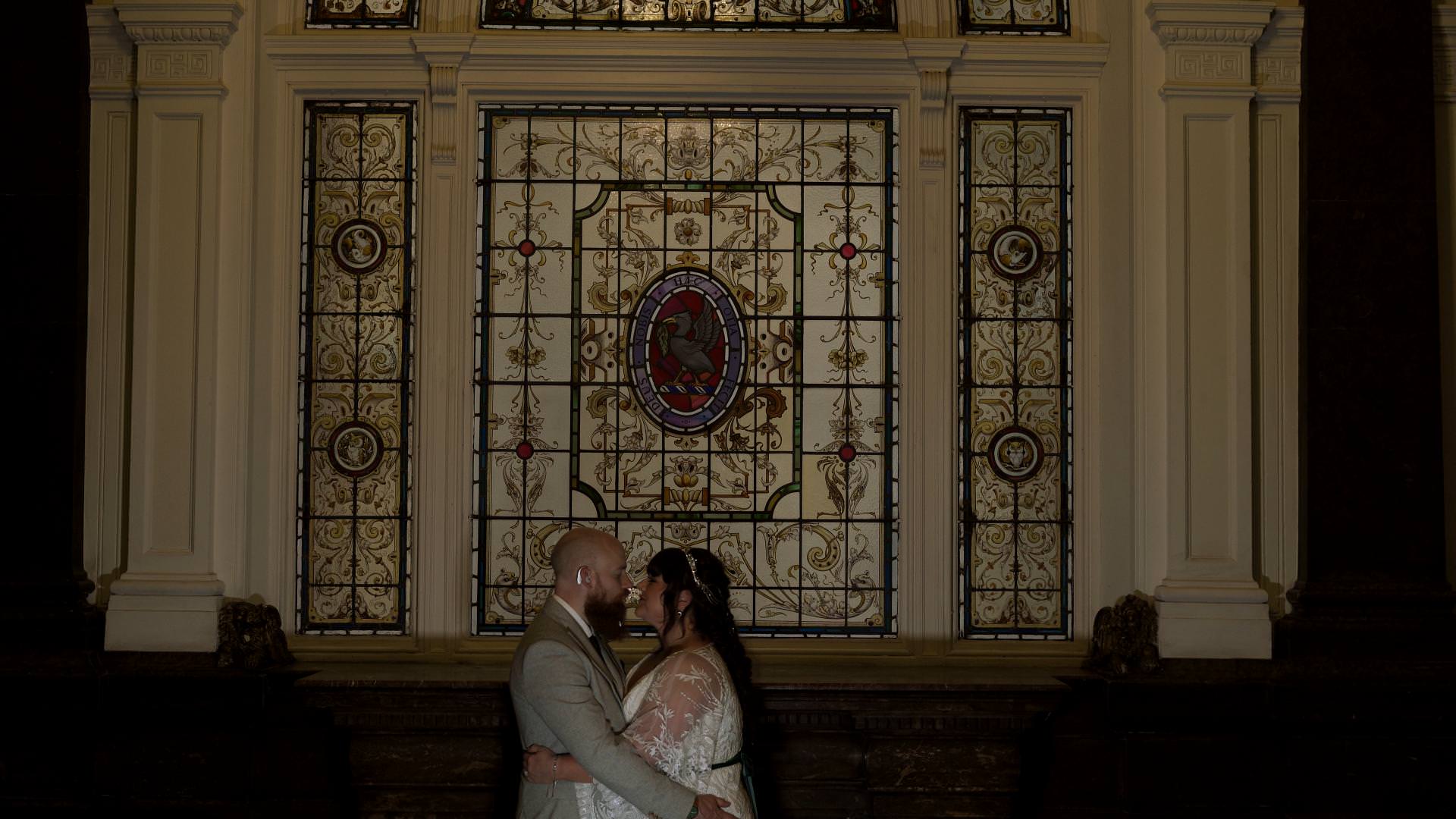 couple pose under stained glass window in Corinthian Grand