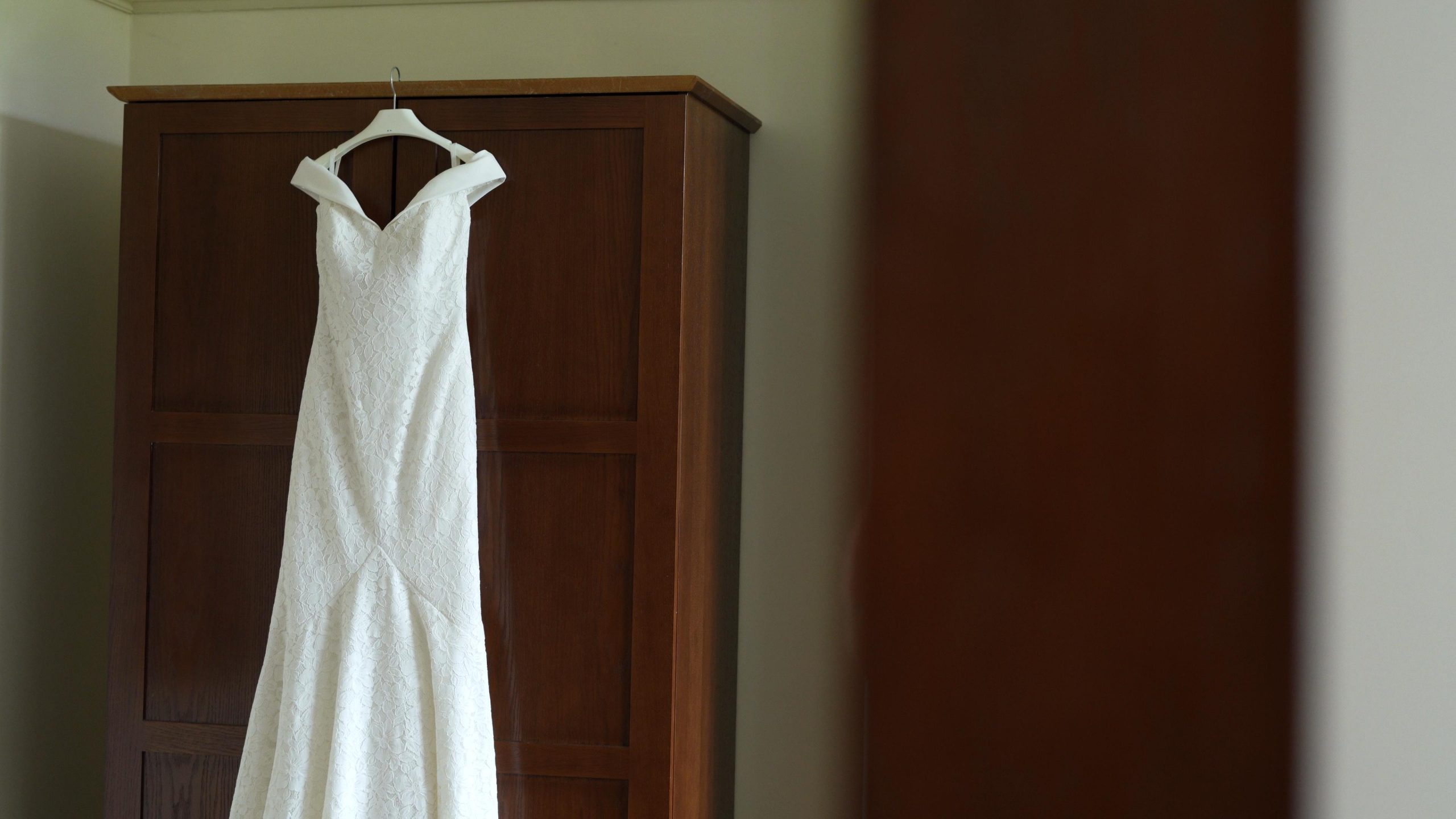 off shoulder wedding dress hangs on wardrobe