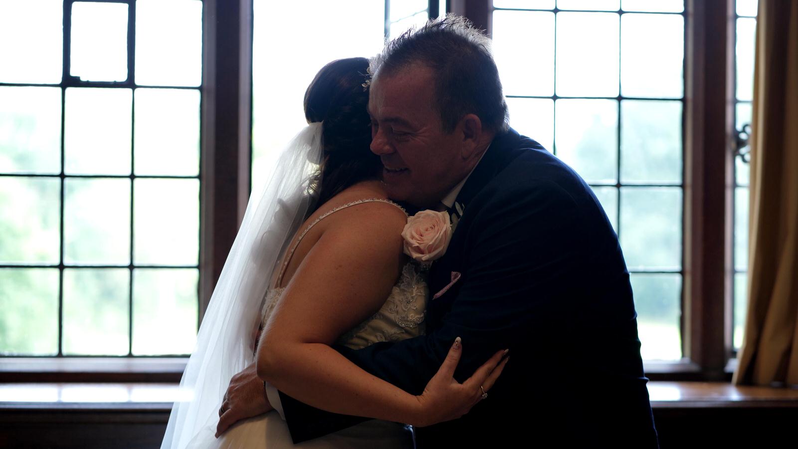 dad hugs bride in front of bright window