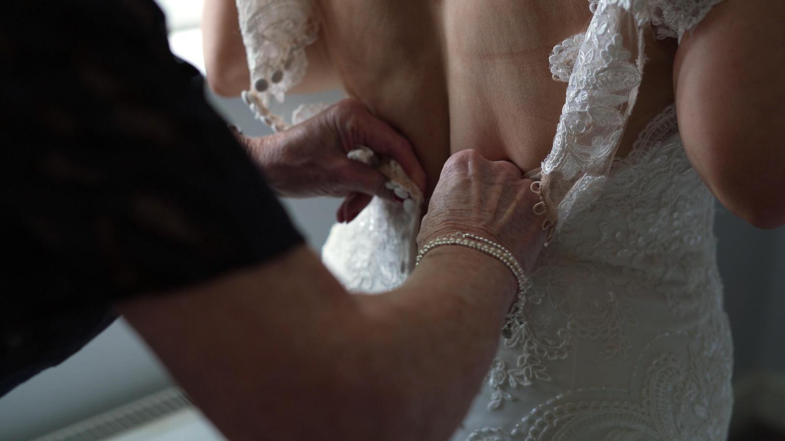 brides mum helps her fasten her wedding dress