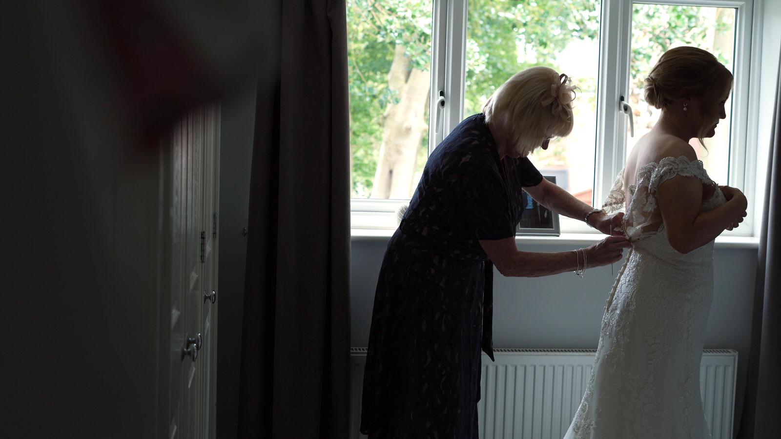 videographer films bride getting help in to her wedding dress