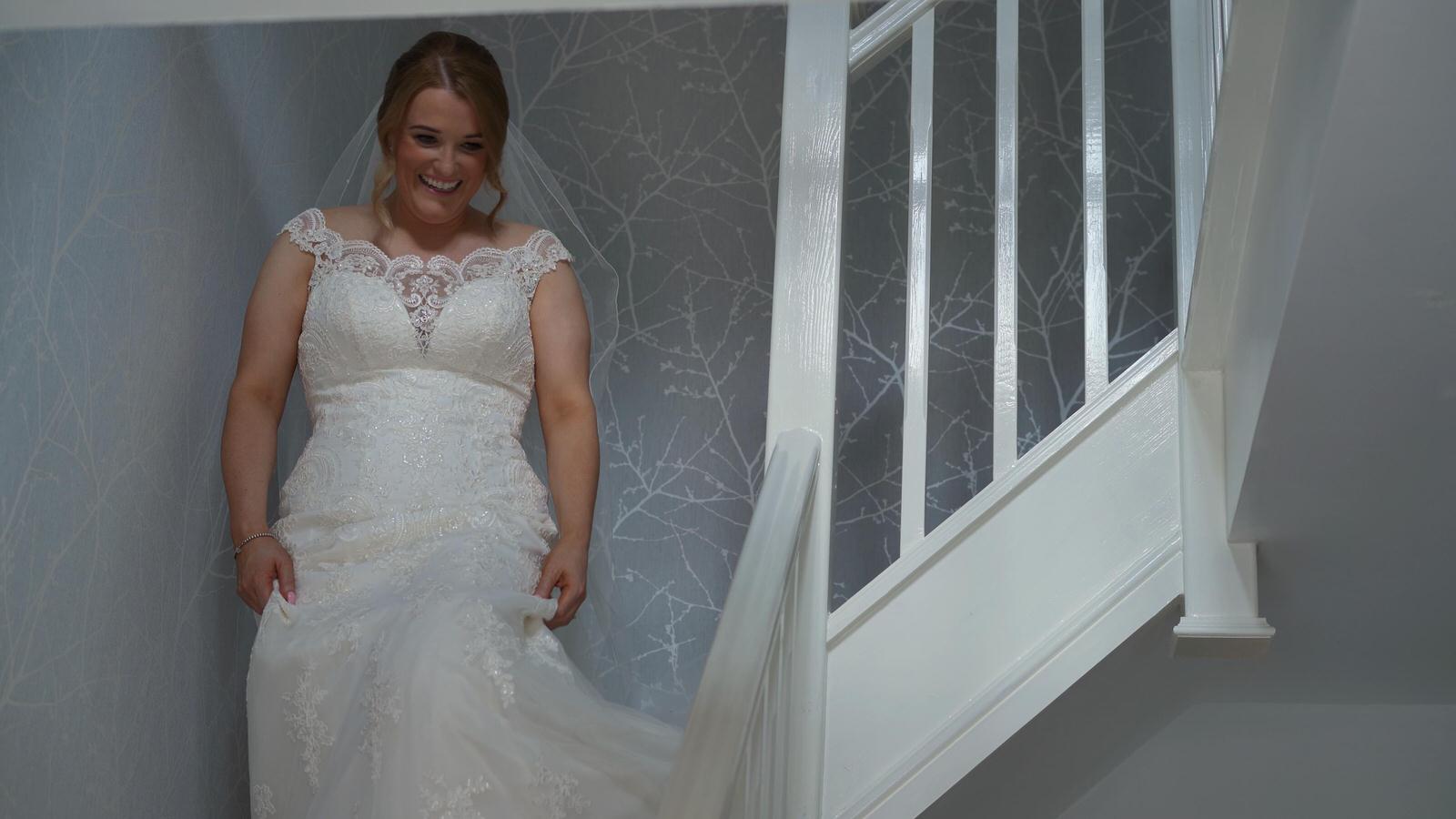 bride in wedding dress walks down stairs at home