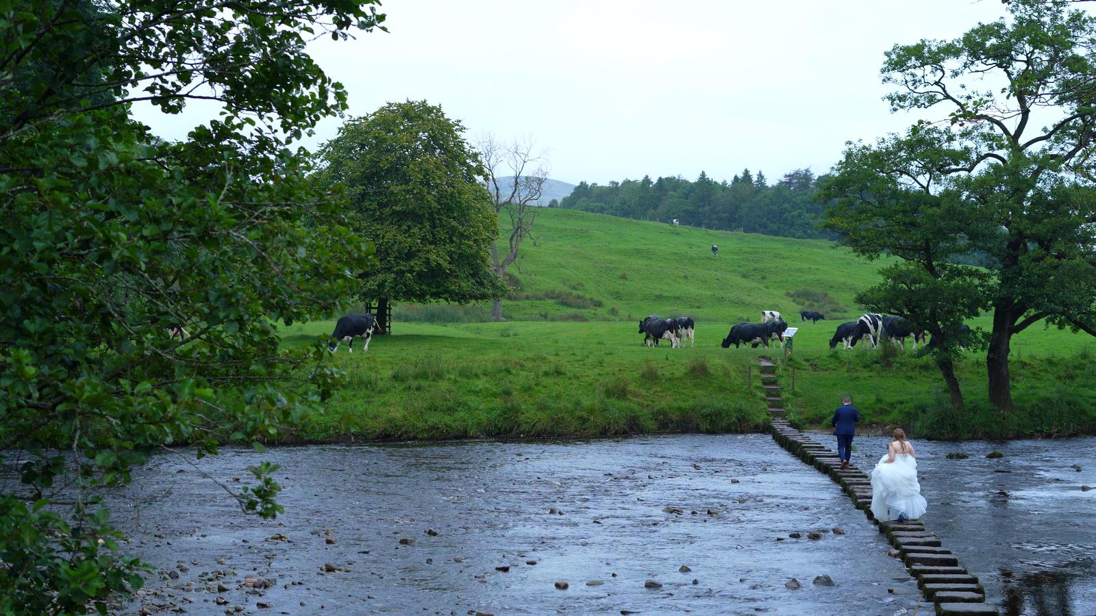 bride and groom walk along stepping stones in Forest of Bowland