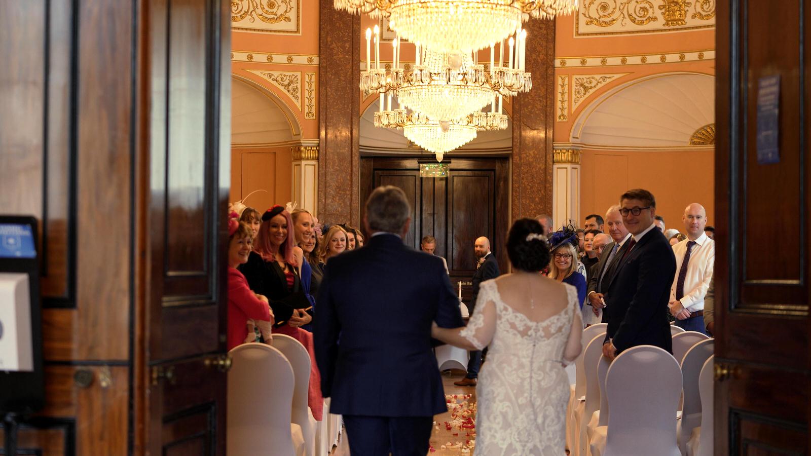 bride walks down the small ballroom aisle at town hall