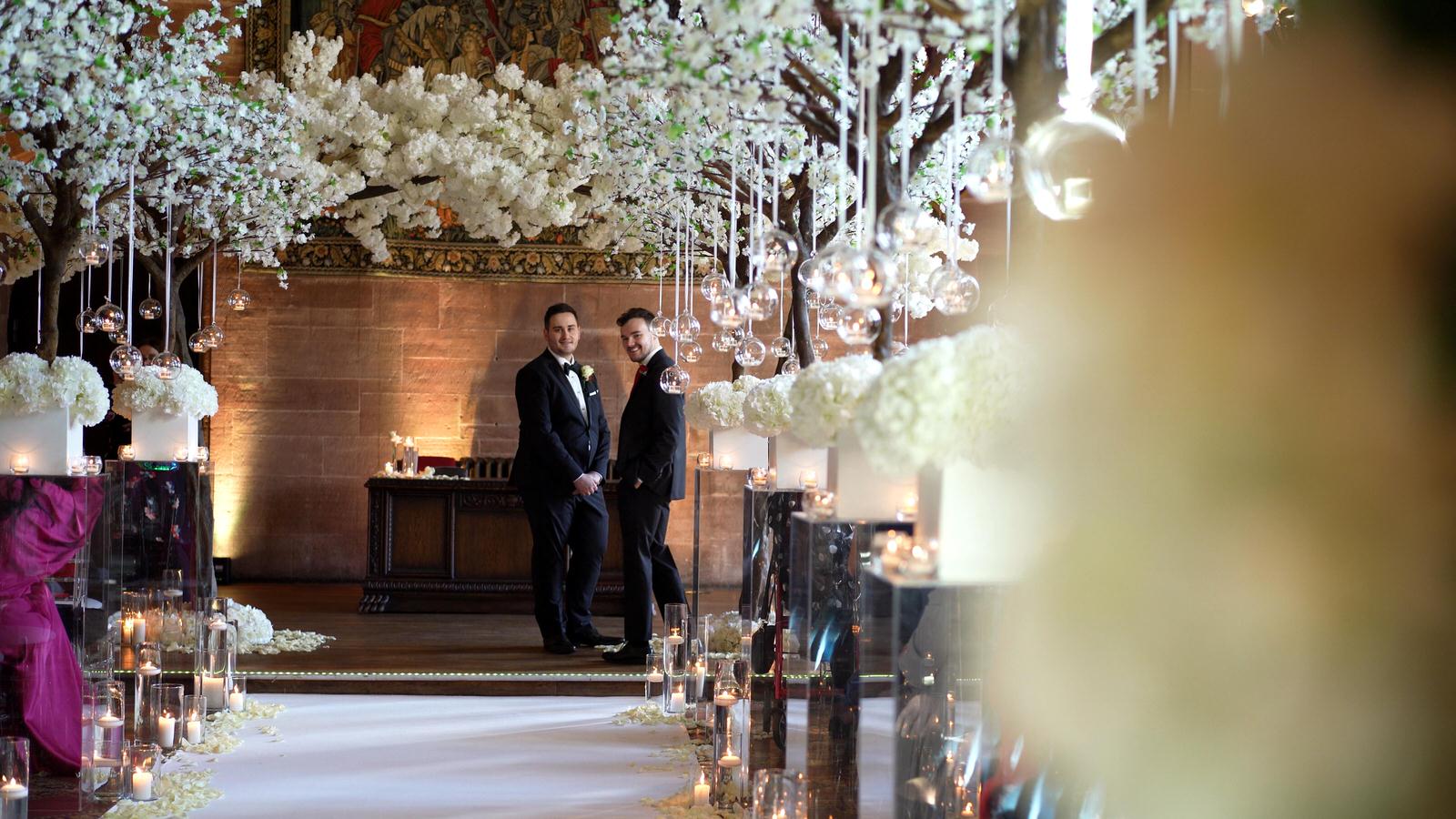 groom looks back up blossom aisle at peckforton castle