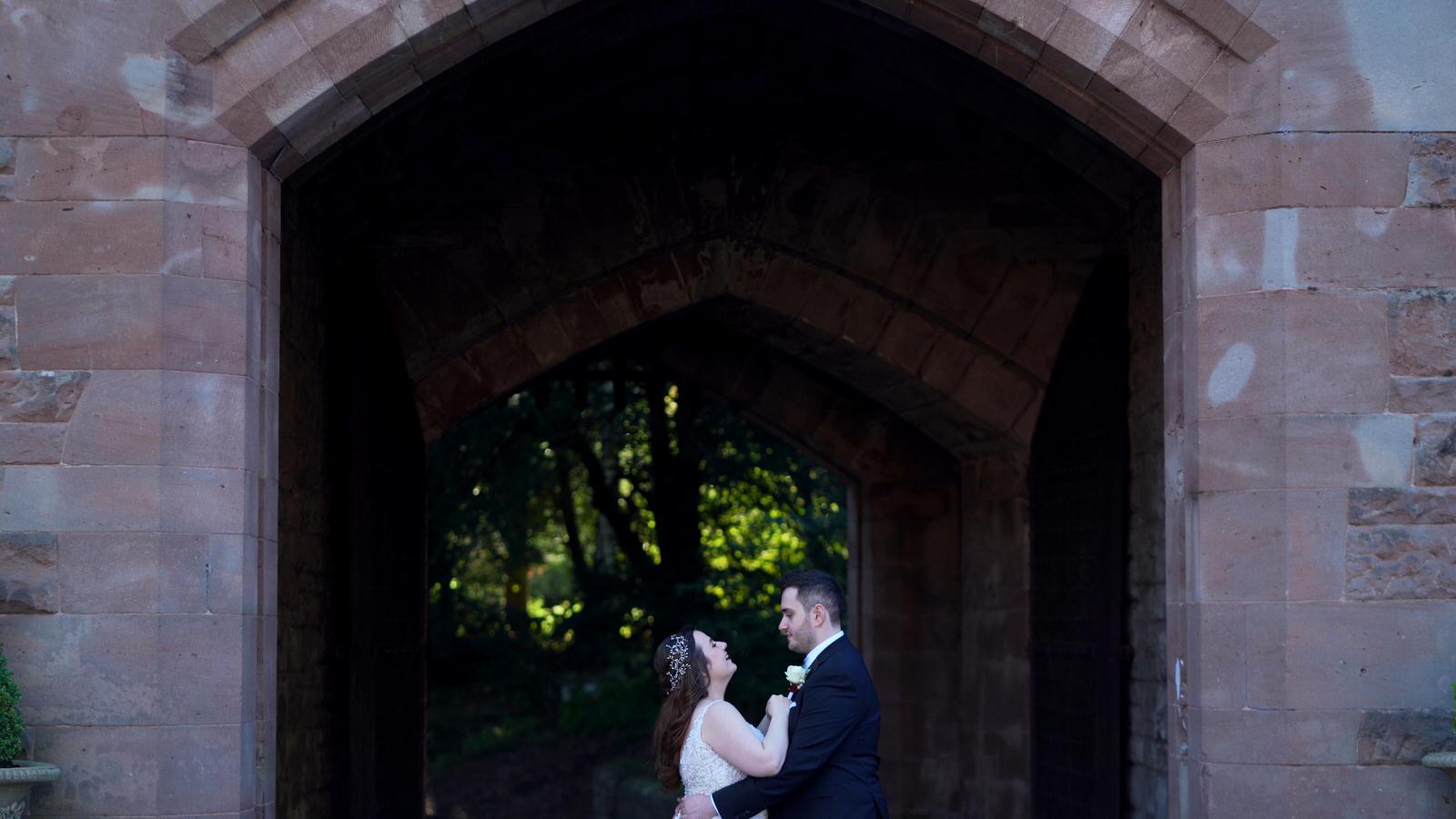 couple snuggle under gateway arch at peckforton castle