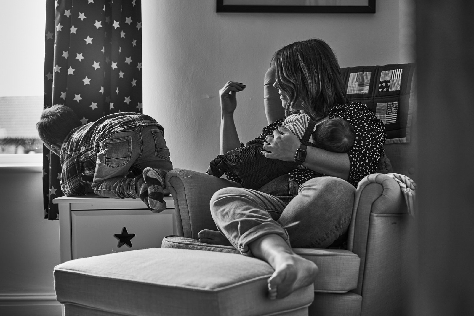 mum breastfeeds baby whilst watching toddler climb at home