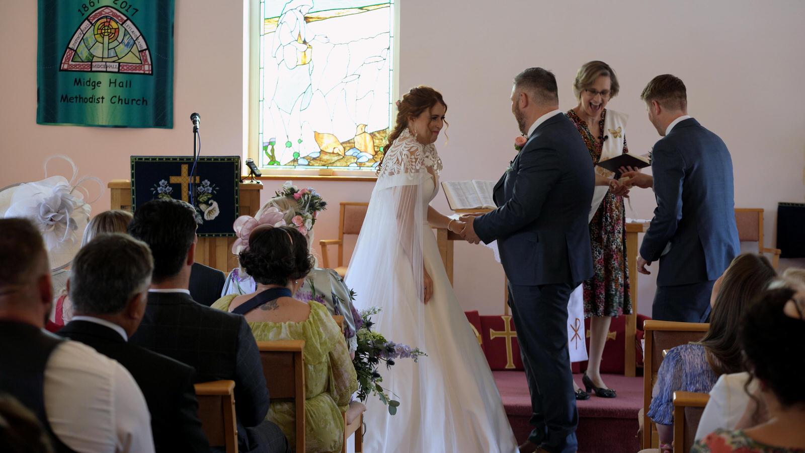 the bride and priest laugh during ceremony at Midge Hall church