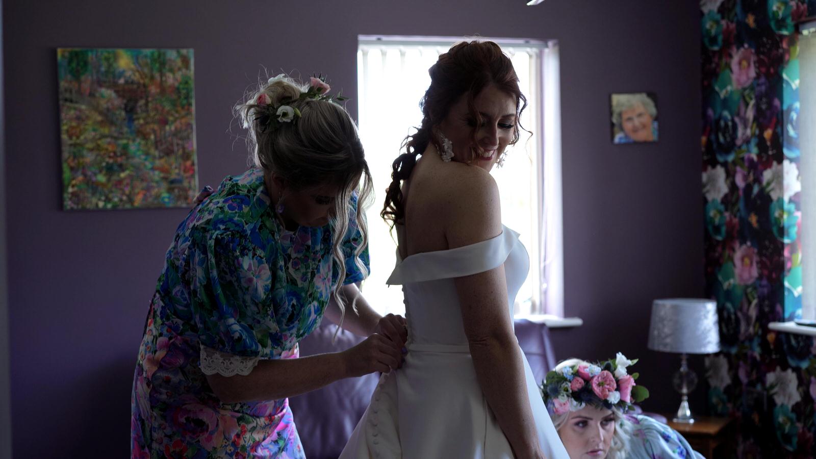 bridesmaids help bride get dressed in her parents lounge