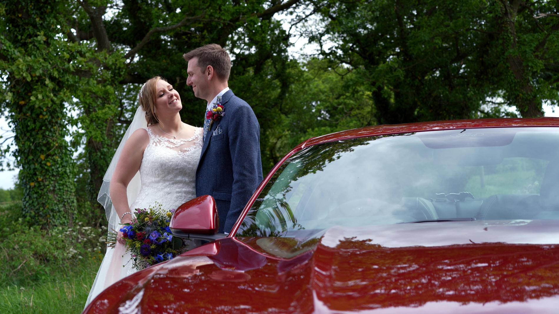 couple smile next to Shabang red ford Mustang car