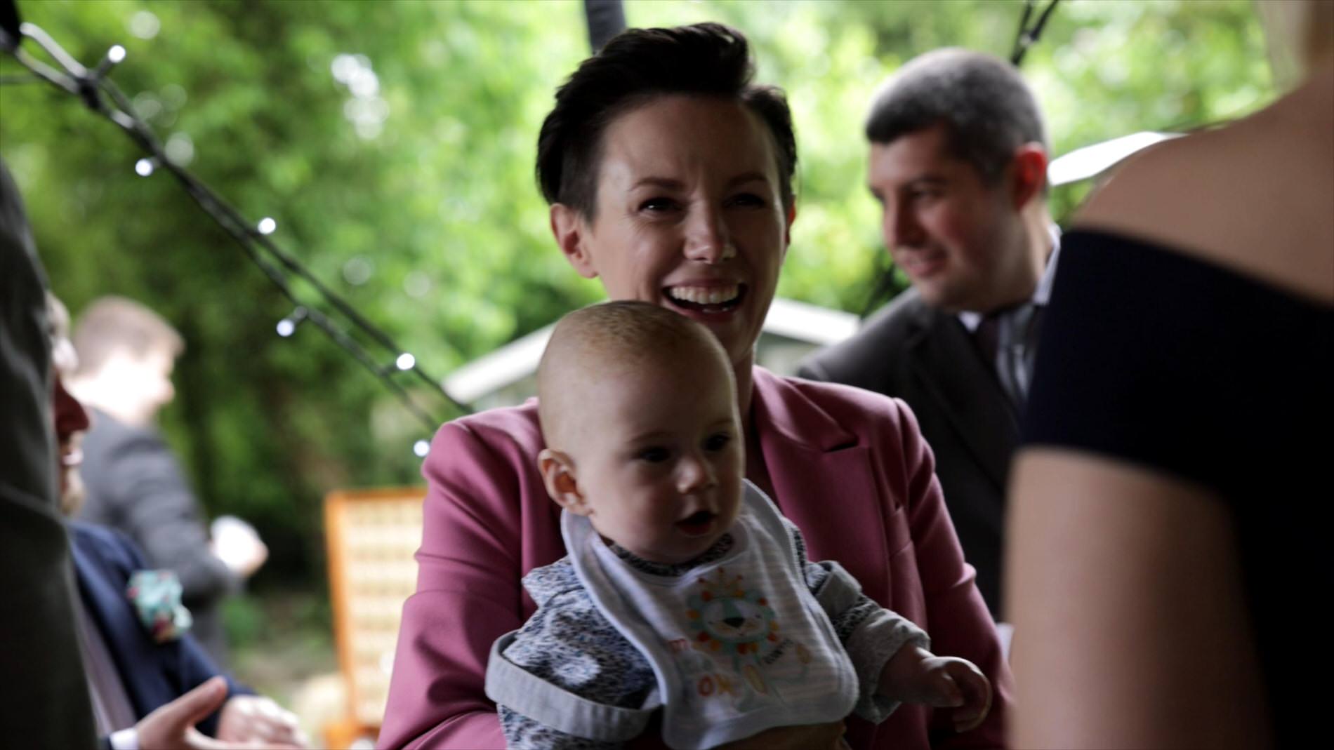 videographer holds baby during wedding reception