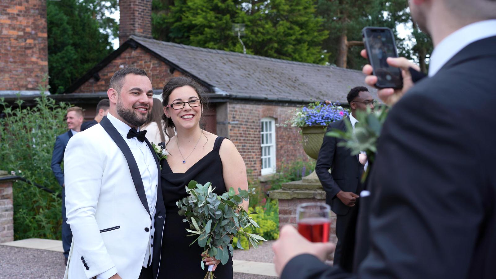 groom poses for a phone photo with sister