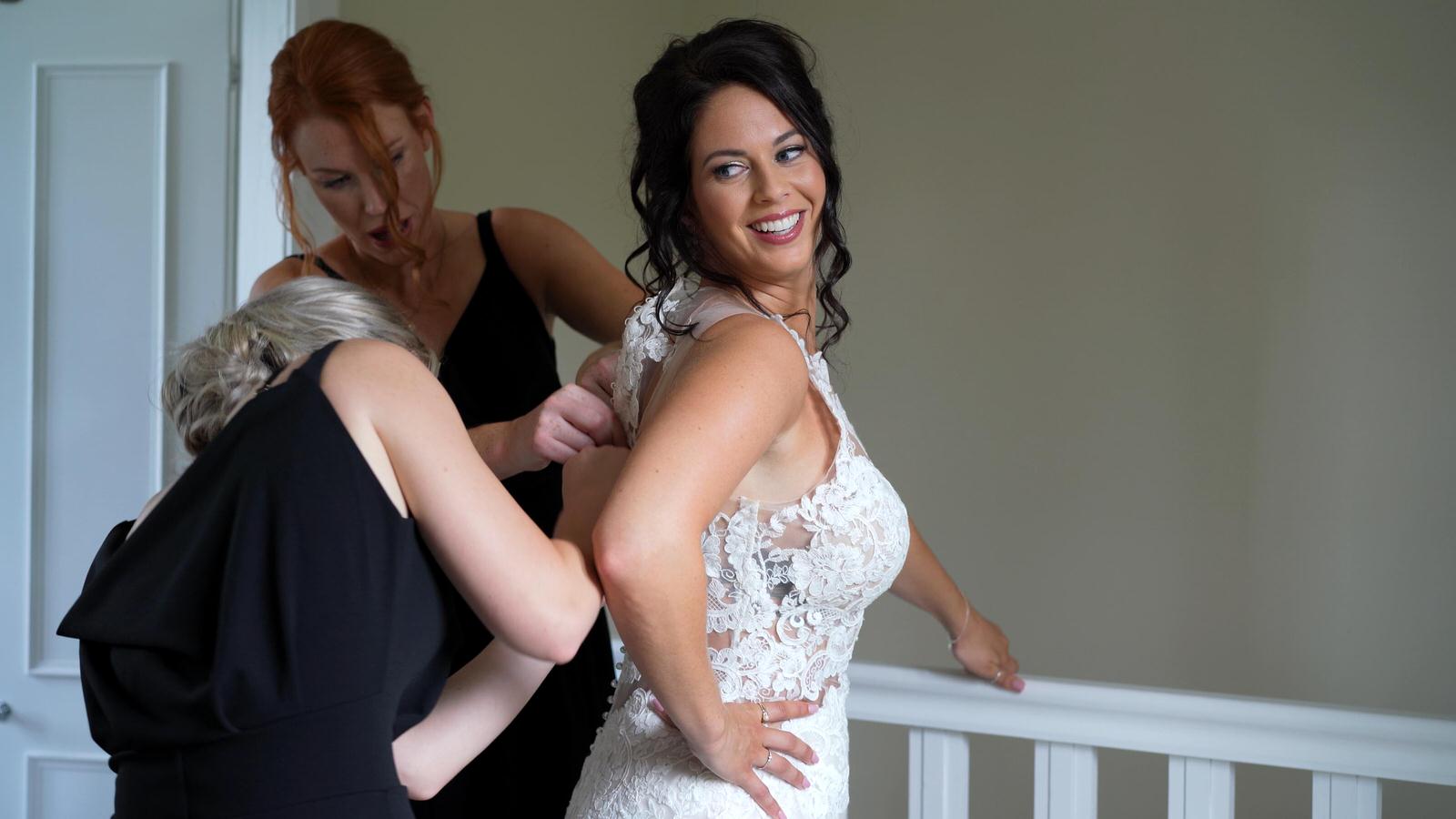 bridesmaids help the bride get in to her wedding dress at Capethorne