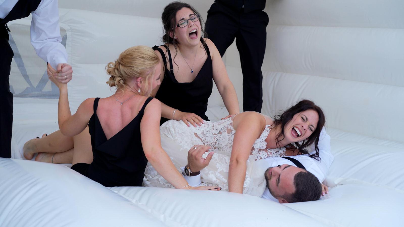guests pile on bride and groom on white bouncy house