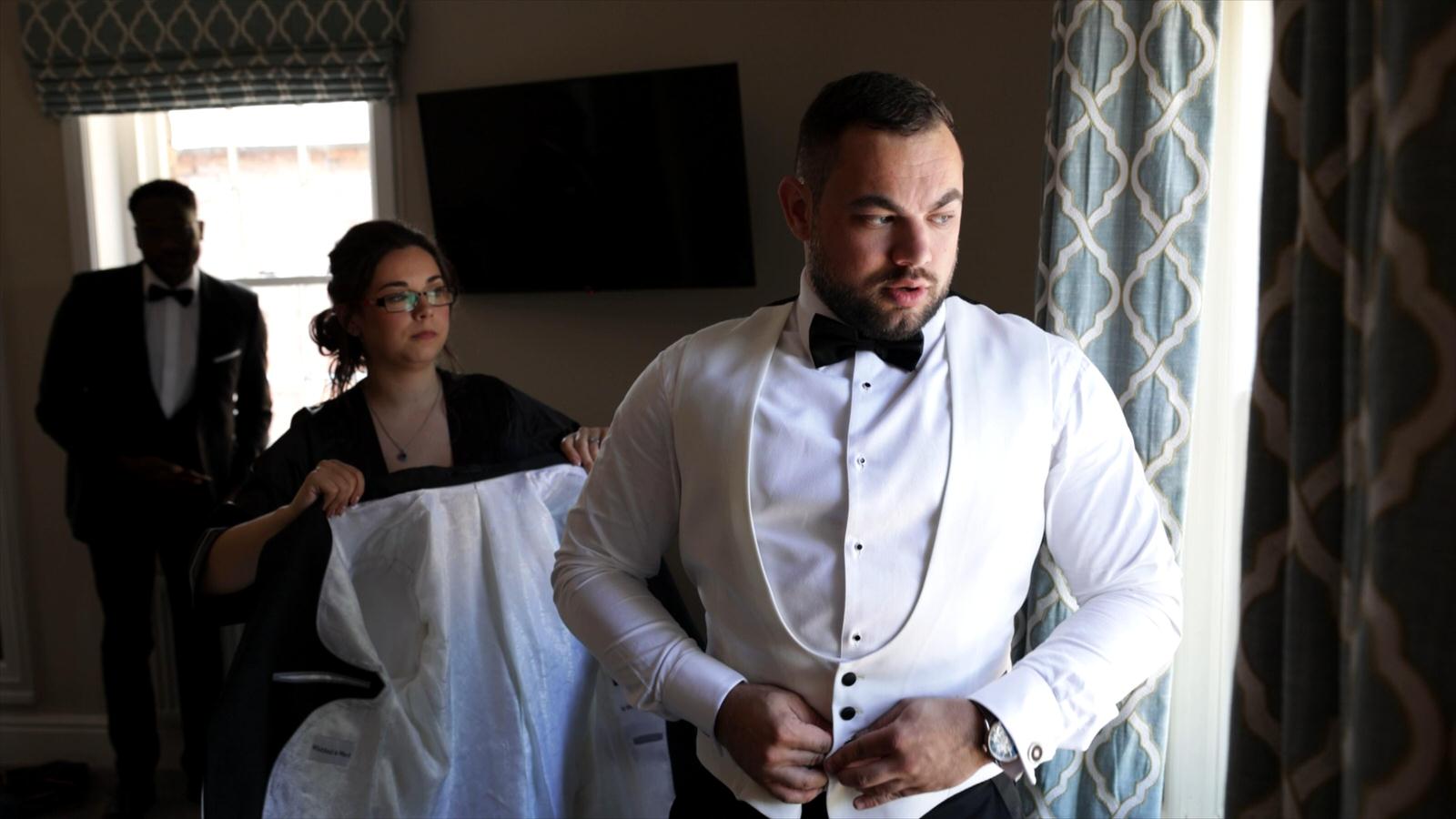 a groom fastens his white tuxedo waistcoat