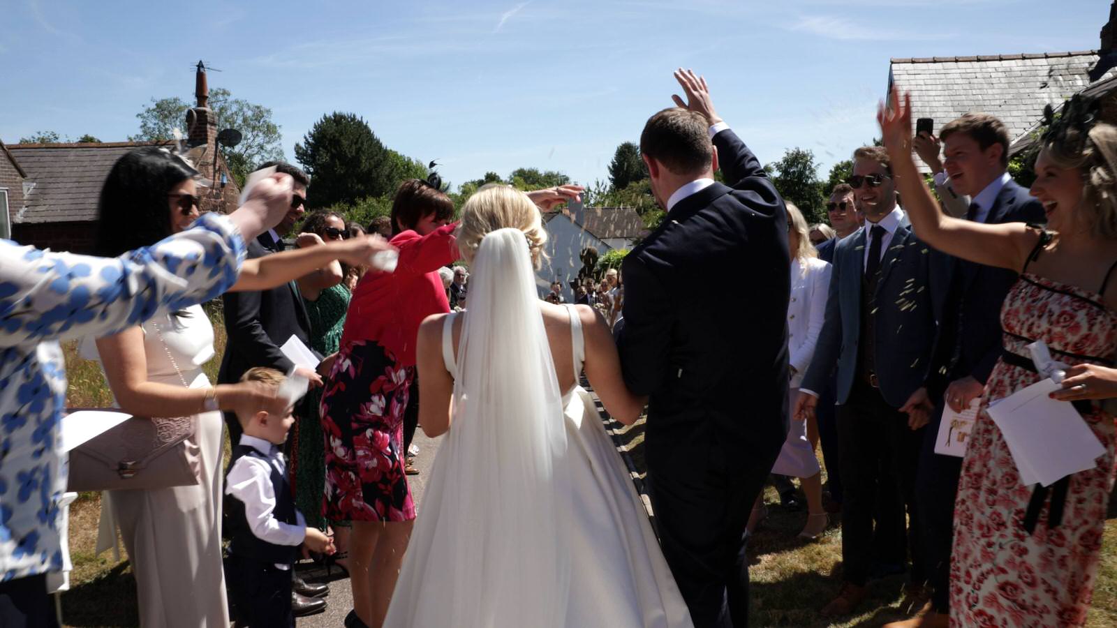 videographer films couple walking in to confetti line